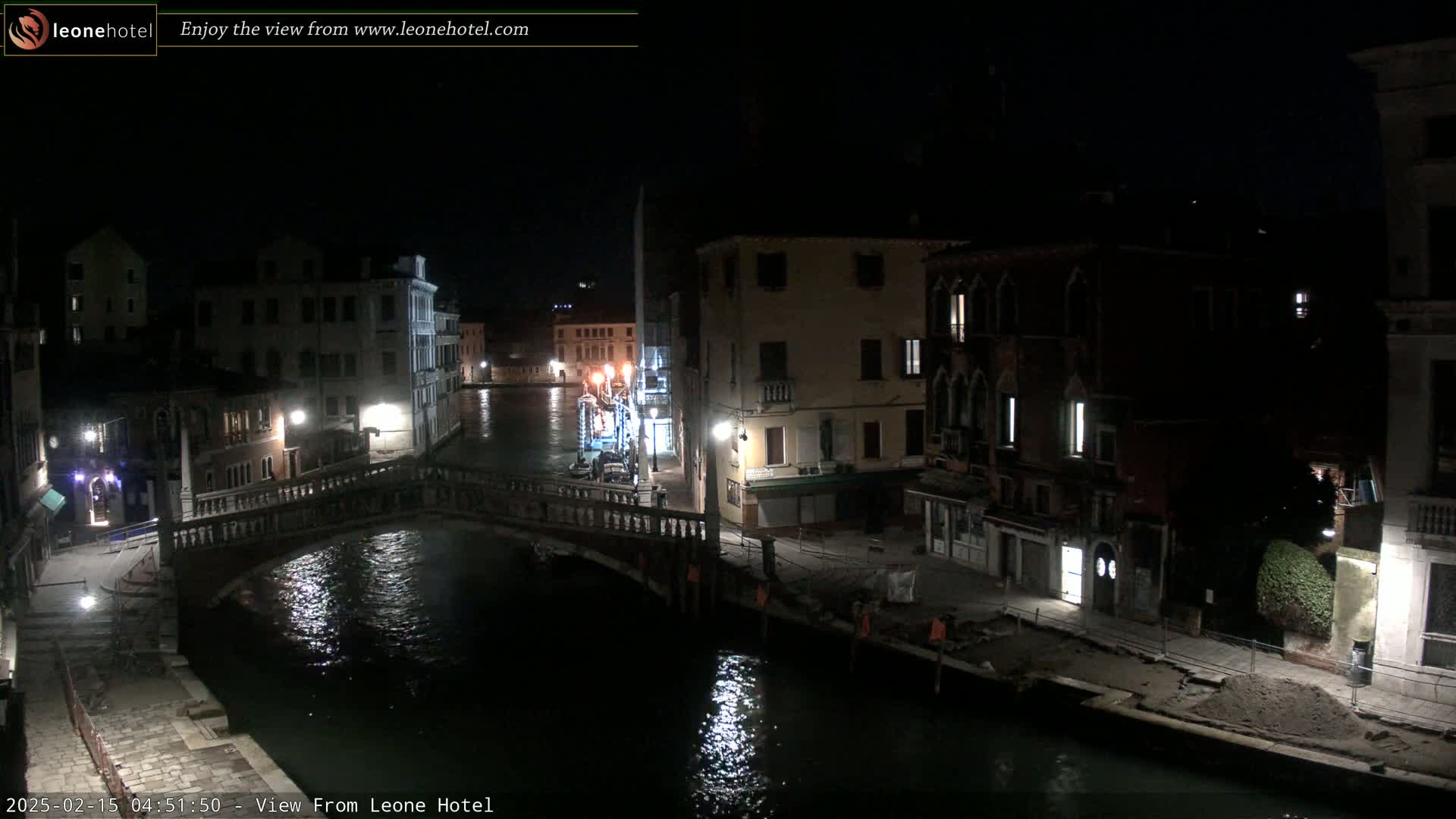 A nighttime view of a canal in Venice, Italy, shows several buildings lining the waterway and a bridge spanning the canal.