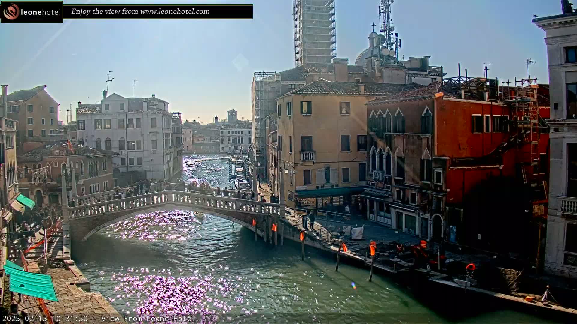 A sunny day in Venice shows a canal with a bridge crowded with people, and colorful buildings lining the waterway.