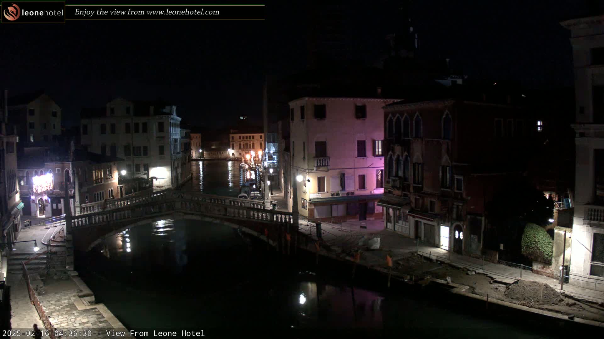 A nighttime view of a canal in Venice, Italy, with several buildings lit along its banks and a bridge crossing the water.