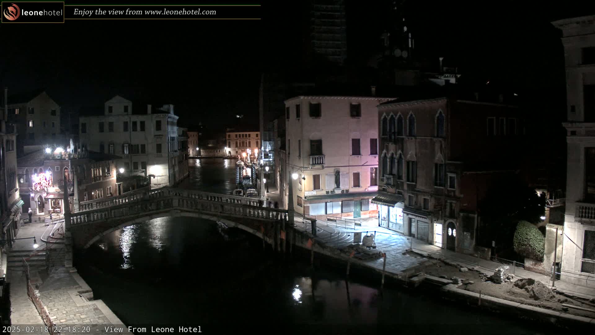 A nighttime view of a canal in Venice, showing buildings lining the waterway and a bridge spanning the canal.
