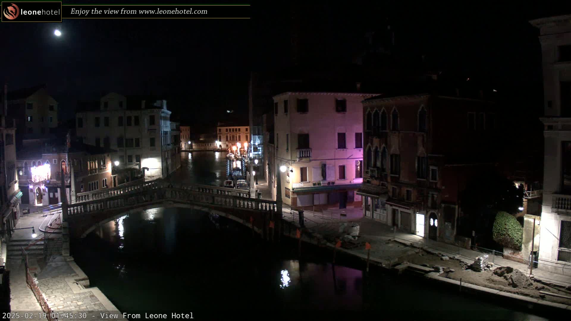 A nighttime view of a canal in Venice, Italy, shows a bridge and several buildings under a moonlit sky.