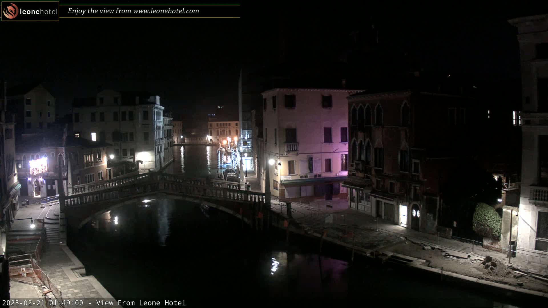 A nighttime view of a canal in Venice, showing several buildings and a bridge, under a clear, dark sky.
