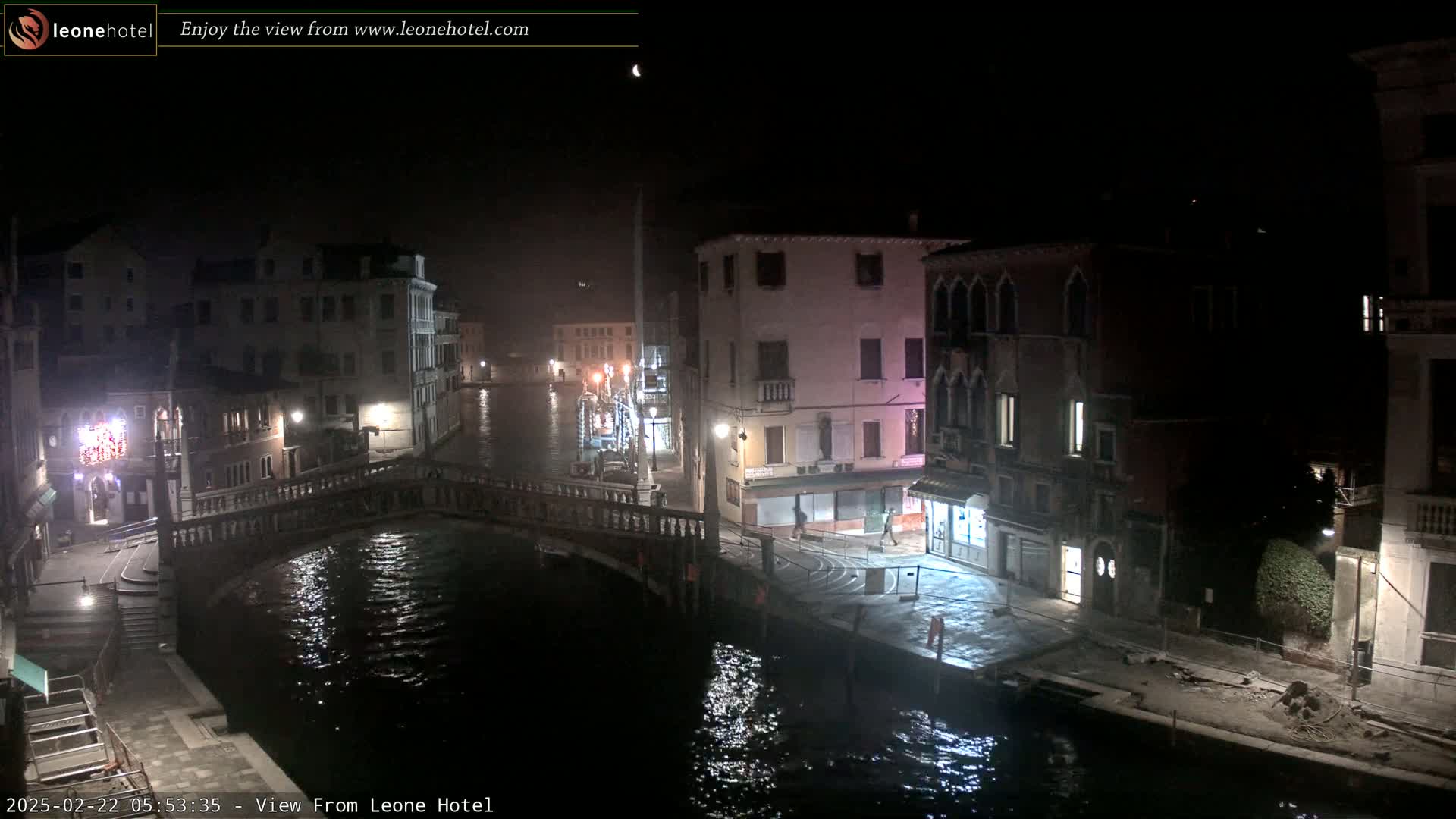 A nighttime view of a canal in Venice, showing buildings lining the waterway and a bridge spanning the canal.