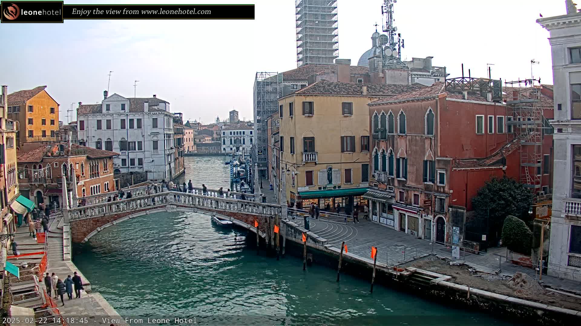 A stone bridge spans a canal in Venice, Italy, with overcast skies and numerous buildings lining the waterway, some under construction.