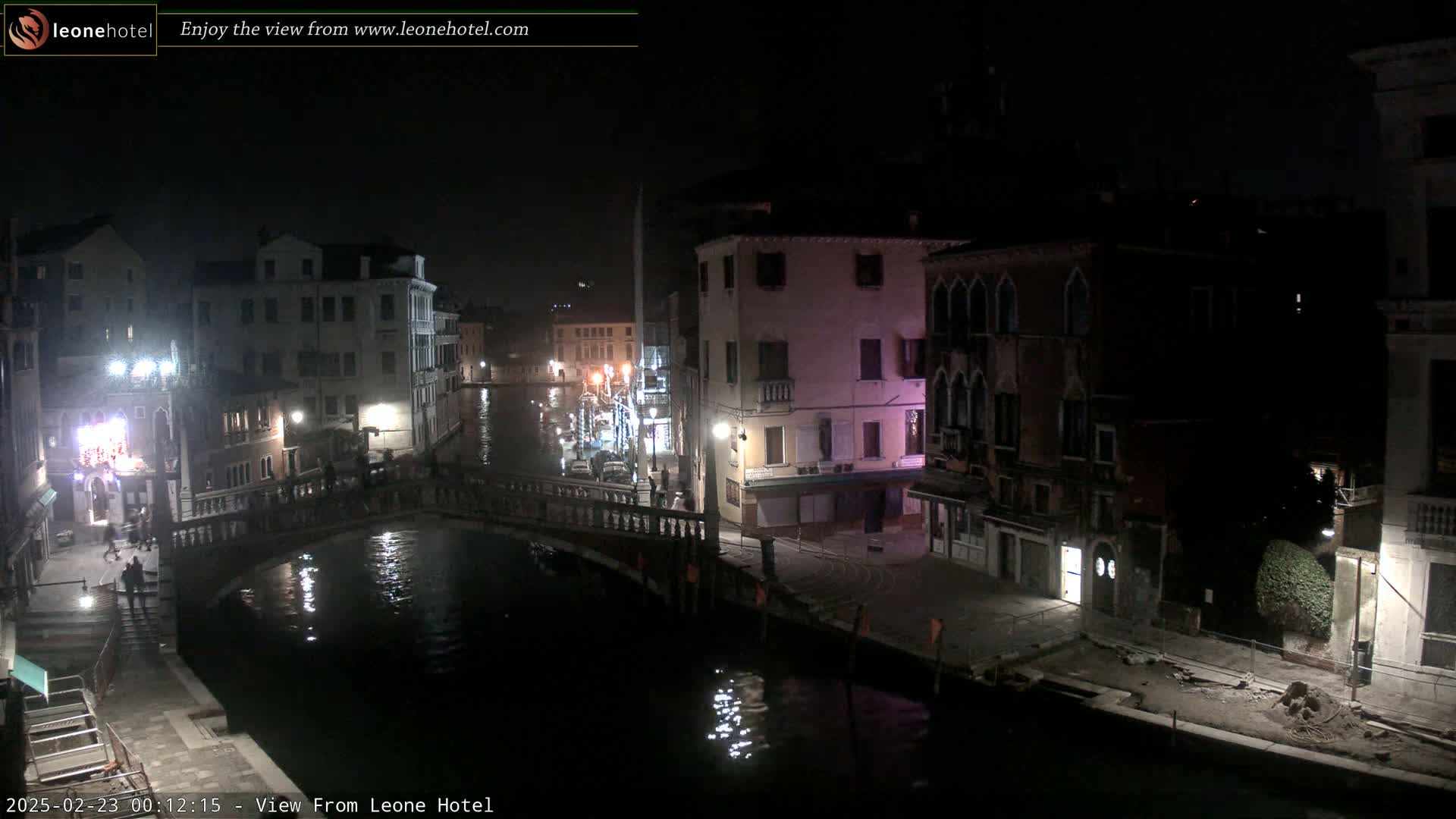A nighttime view of a canal in Venice, with several buildings and a bridge visible, under dark, clear skies.