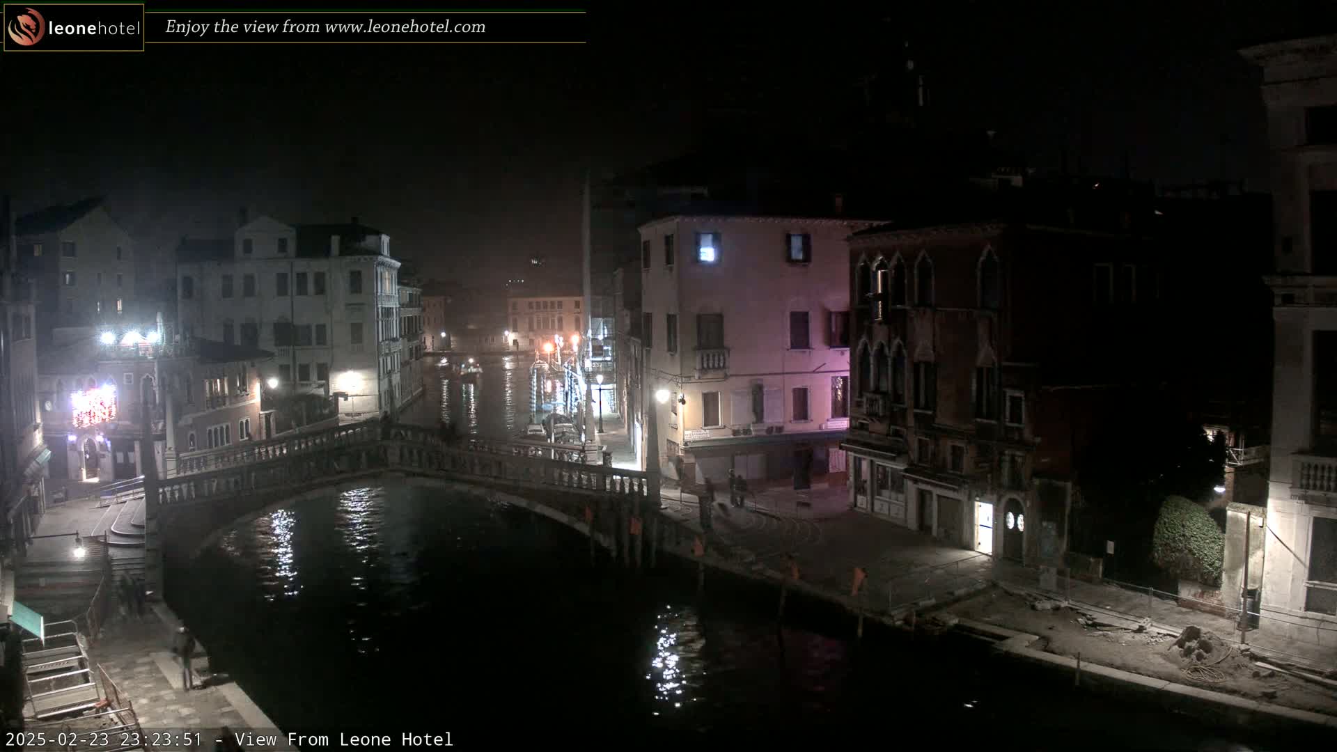 A nighttime view of a canal in Venice, showing bridges, buildings, and a few people, under a dark sky.