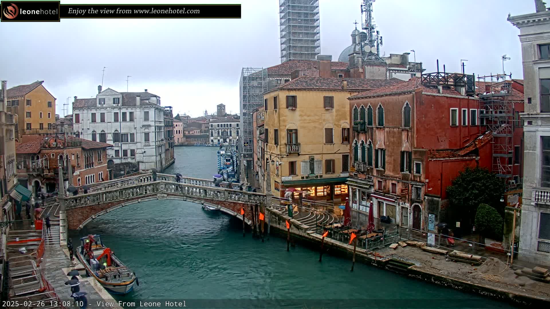 A stone bridge over a canal in Venice, Italy, on an overcast day, with colorful buildings lining the waterway, some undergoing construction.