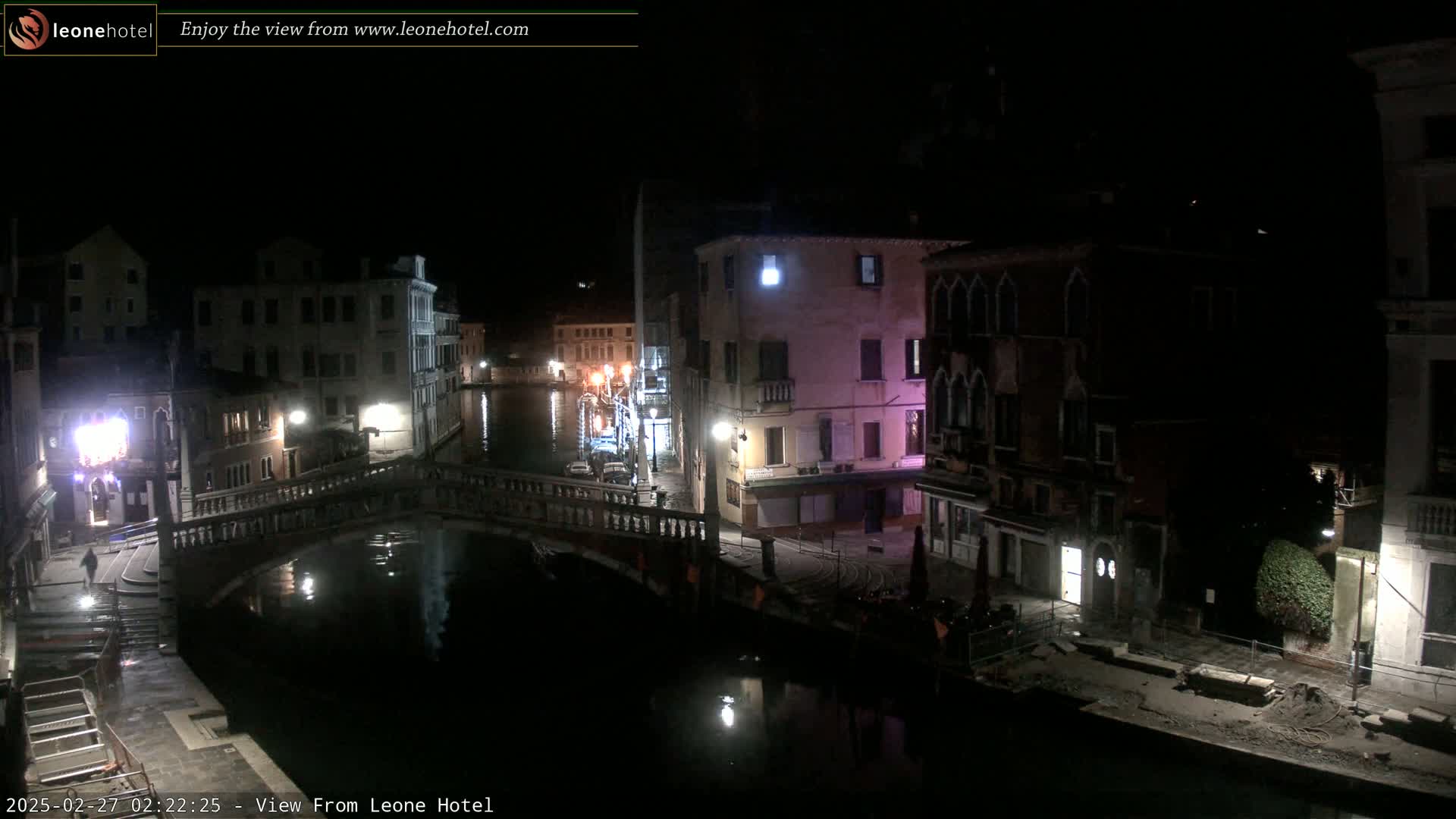 A nighttime view of a canal in Venice, with bridges, buildings, and dimly lit streets.