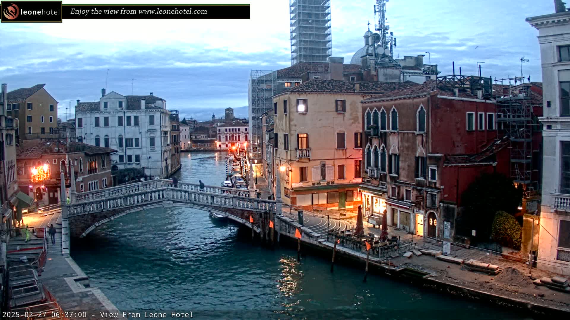 A stone bridge arches over a calm canal in Venice at twilight, with buildings lining the waterway.