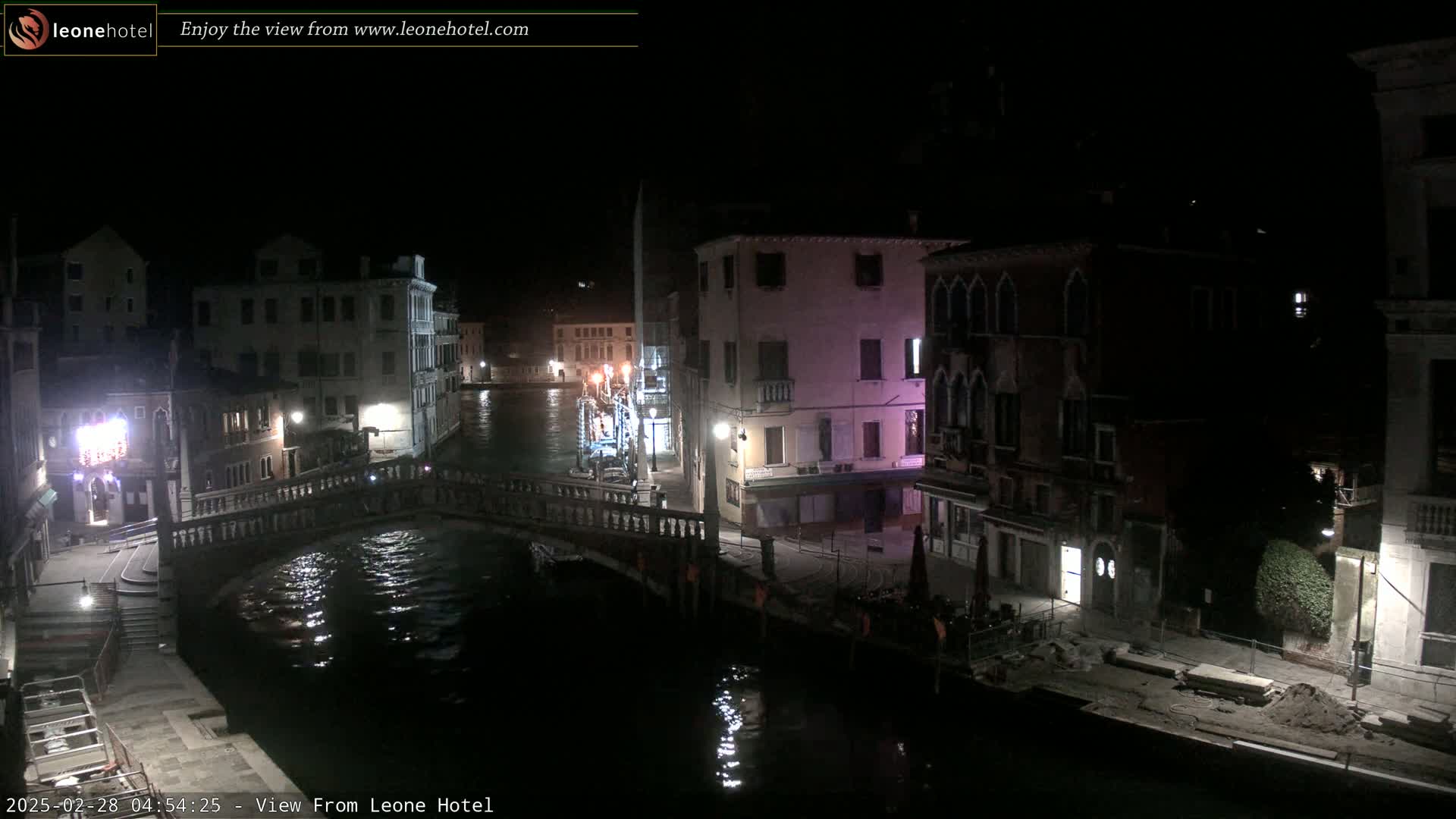 A nighttime view of a canal in Venice, showing several buildings and a bridge, with calm water reflecting the lights.
