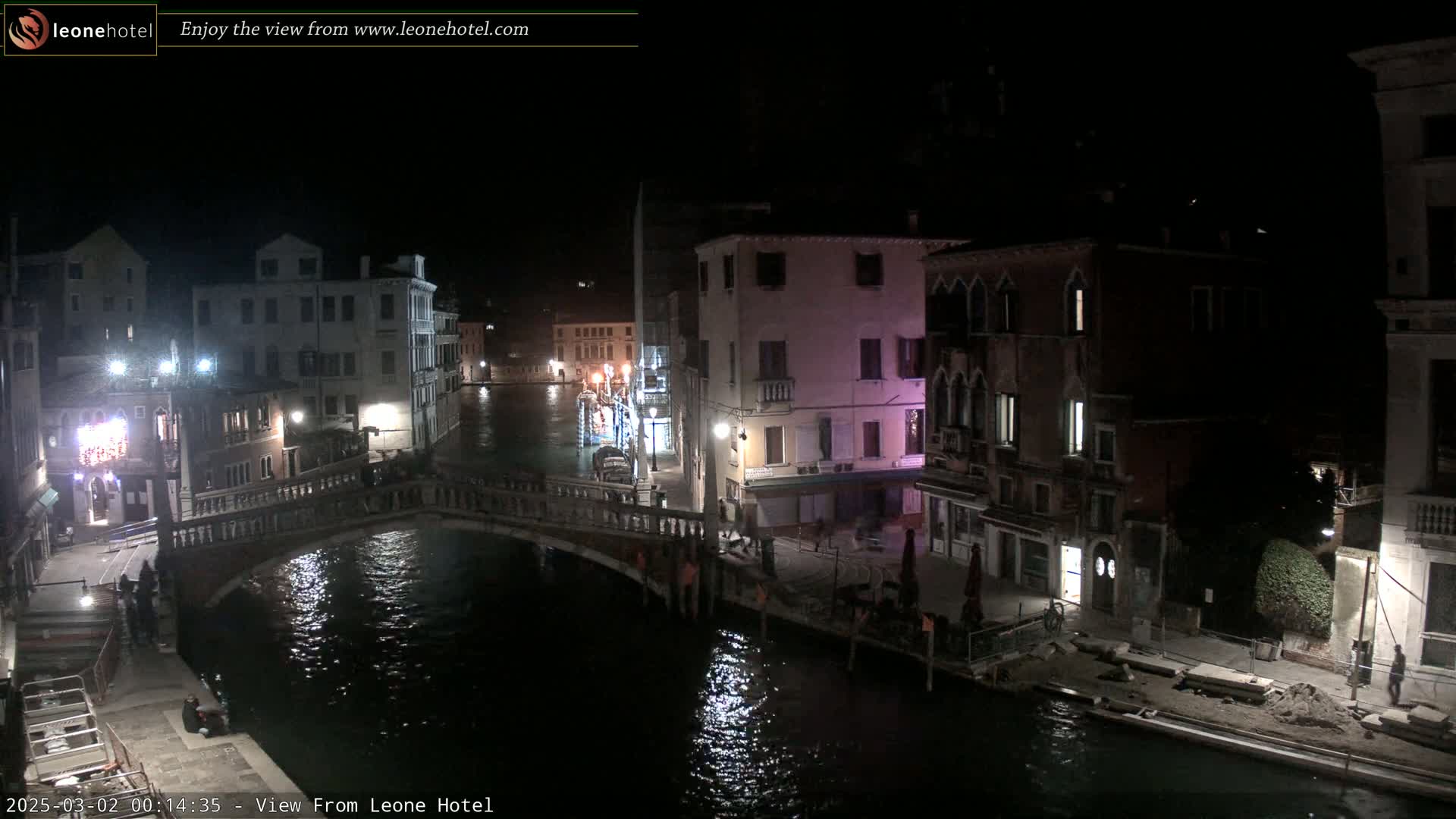 A nighttime view of a canal in Venice, Italy, showing several buildings lining the waterway and a bridge crossing the canal.