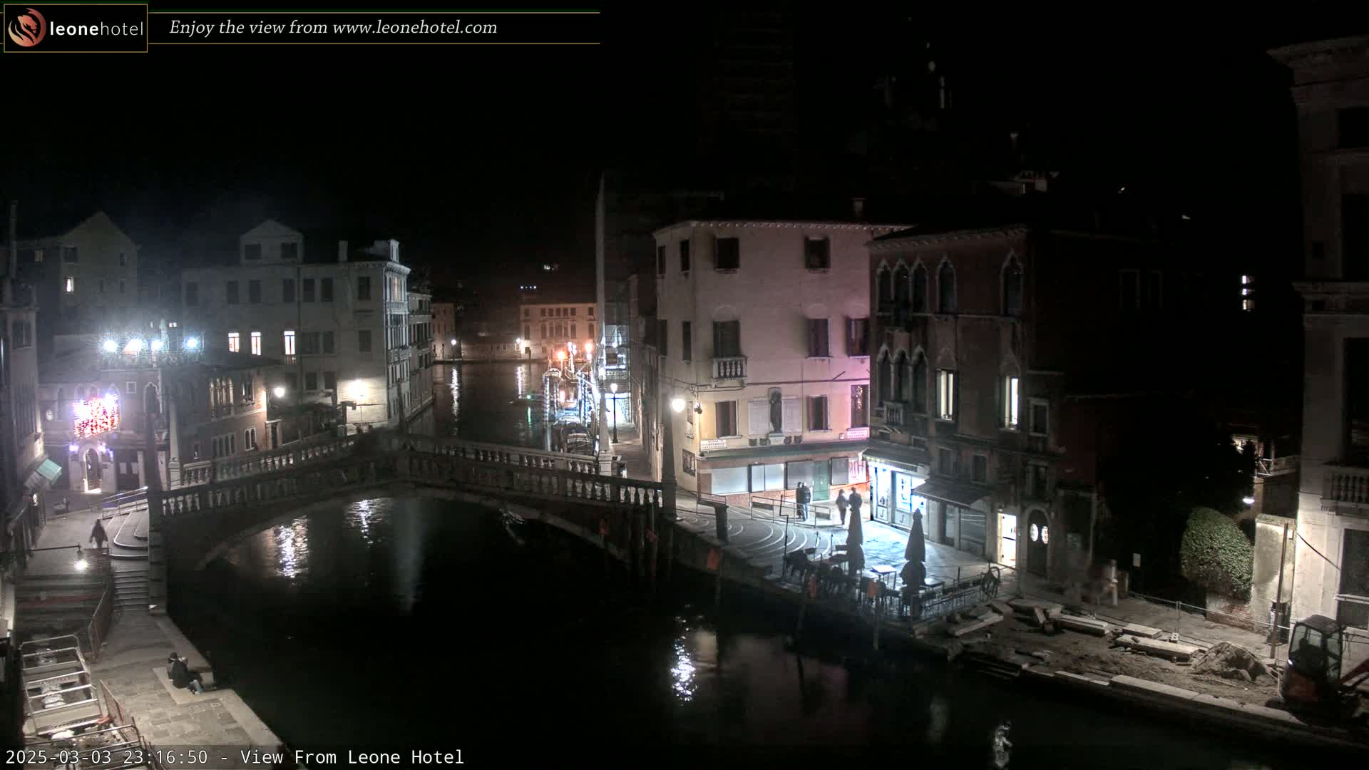 A nighttime view of a canal in Venice, with bridges, buildings, and a few people visible.