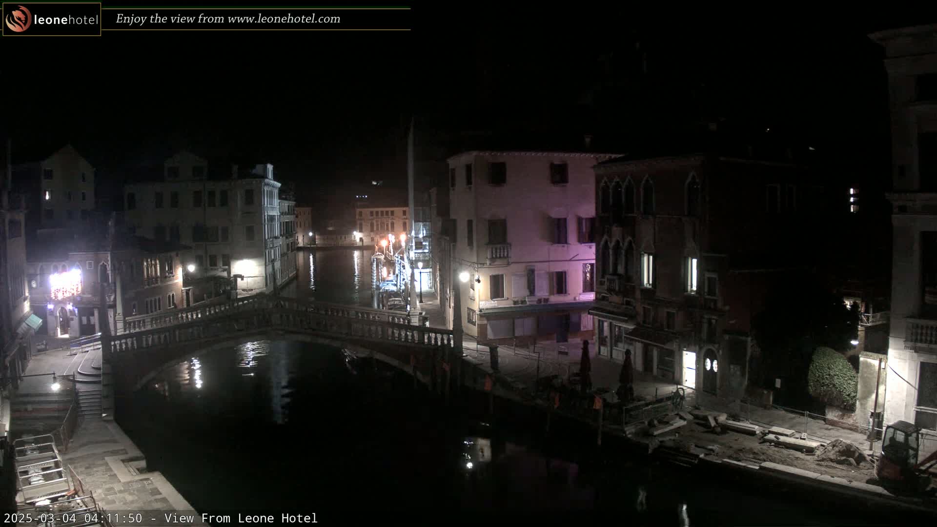 A nighttime view of a canal in Venice, showing bridges, buildings, and some construction activity along the waterway under dark, clear skies.