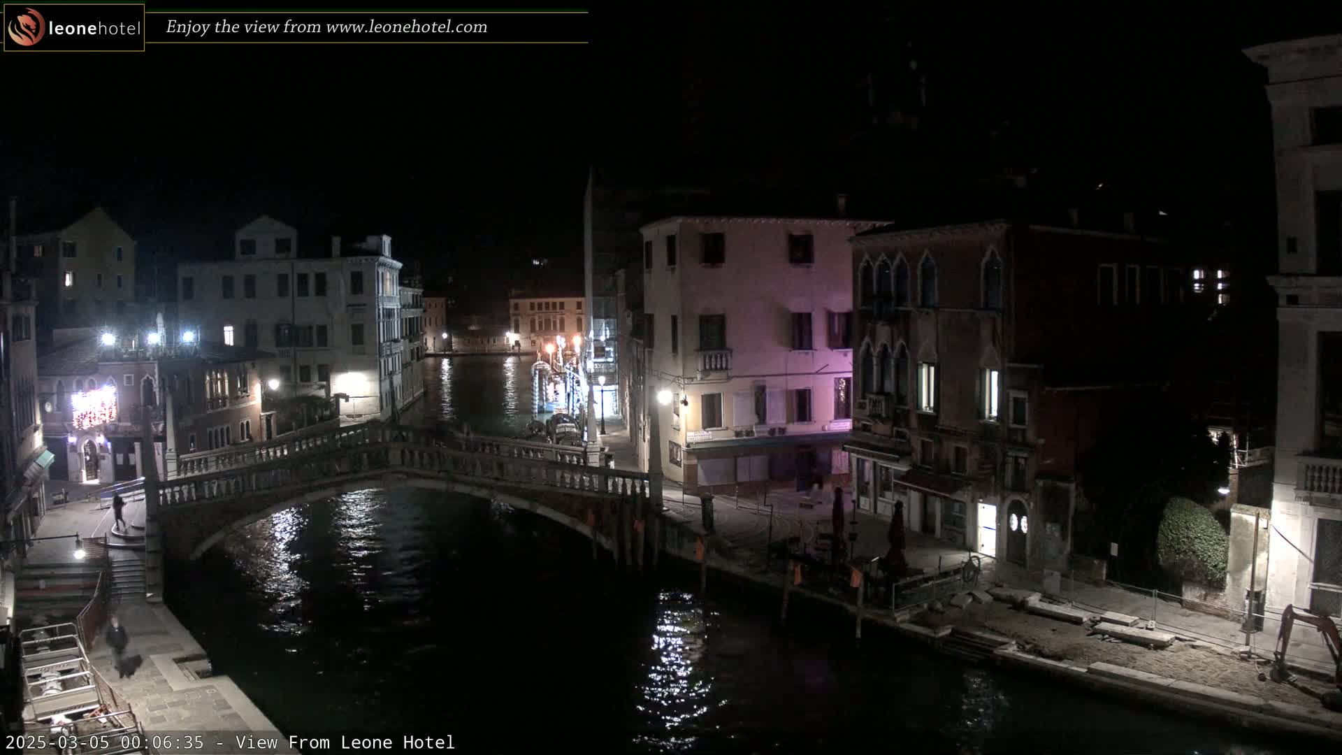 A nighttime view of a canal in Venice, Italy, shows a bridge, buildings lining the waterway, and calm water reflecting lights.
