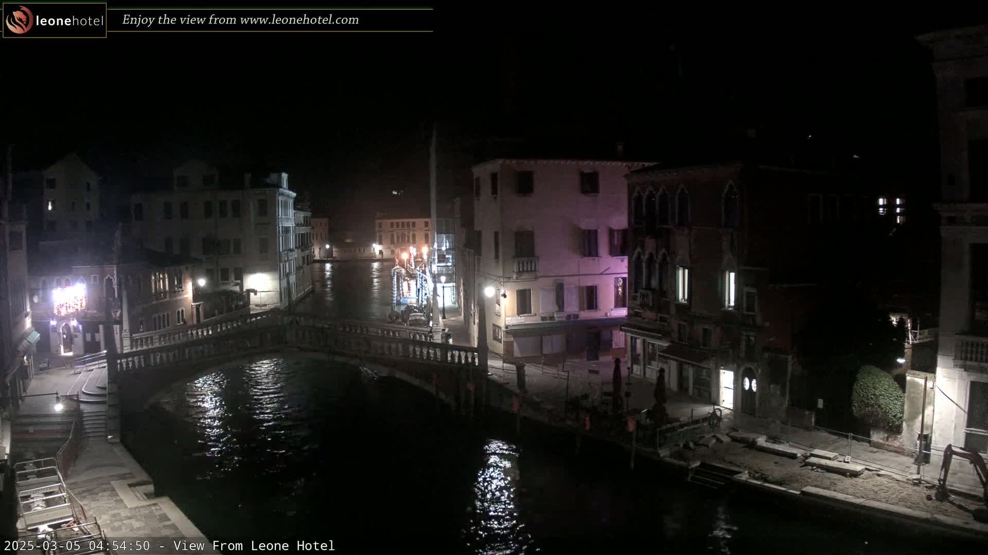 A nighttime view of a canal in Venice, Italy, with bridges, buildings, and some construction along the water's edge.
