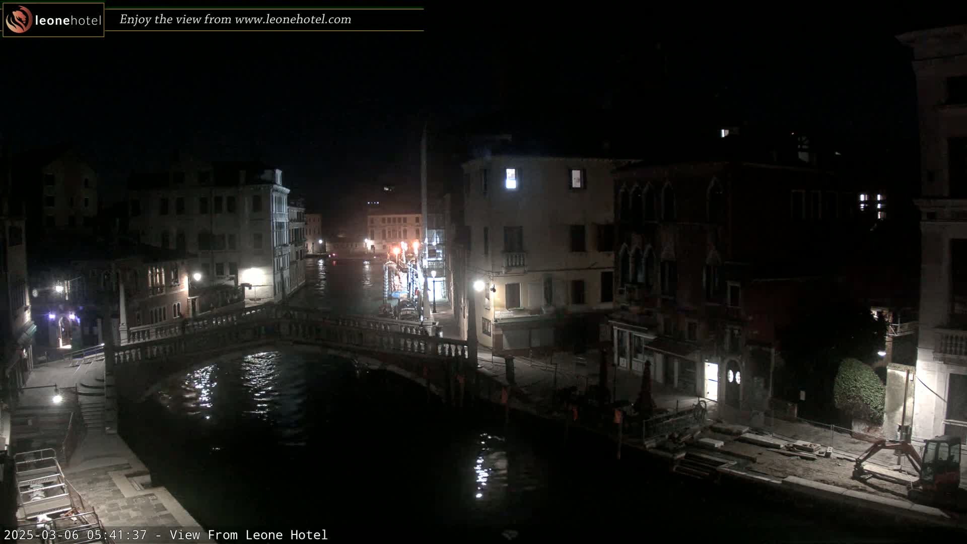 A nighttime view of a canal in Venice, Italy, shows a bridge, several buildings, and a small amount of construction equipment.