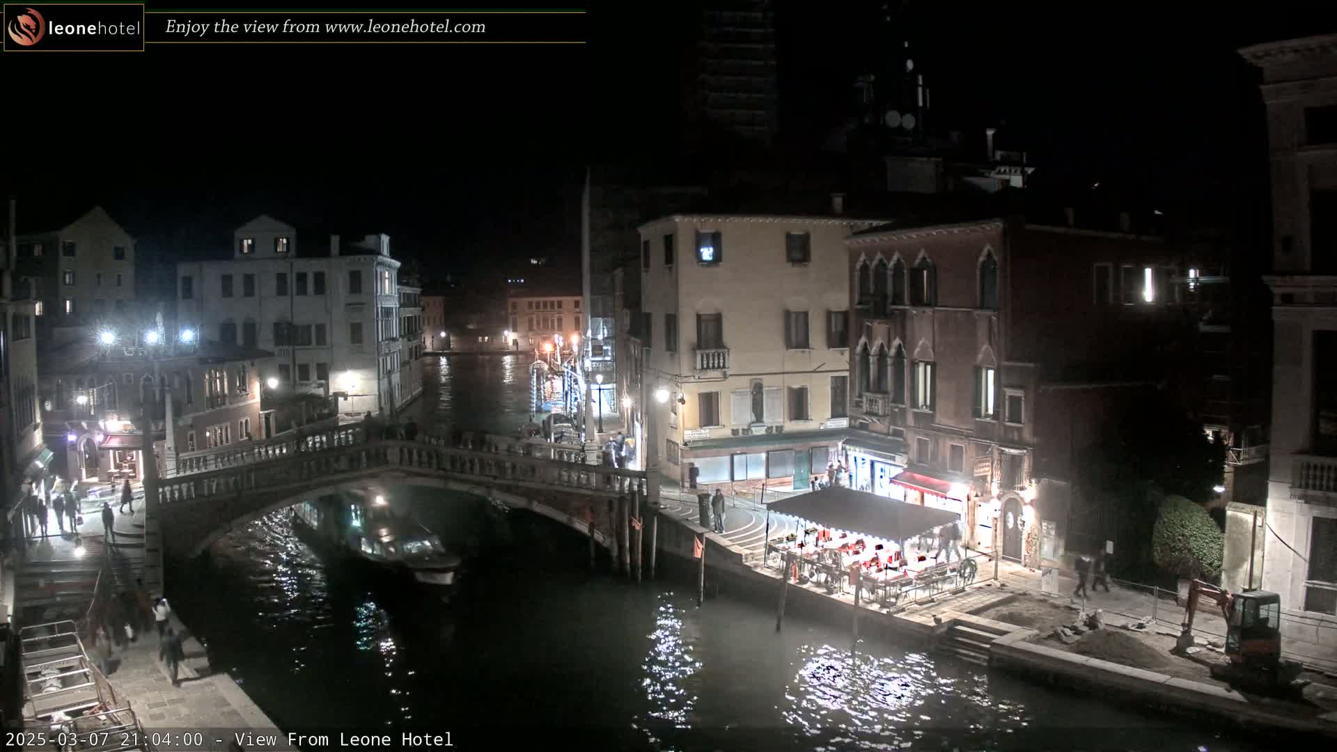 A nighttime view of a Venetian canal with bridges, buildings, and a small boat, under a clear, dark sky.