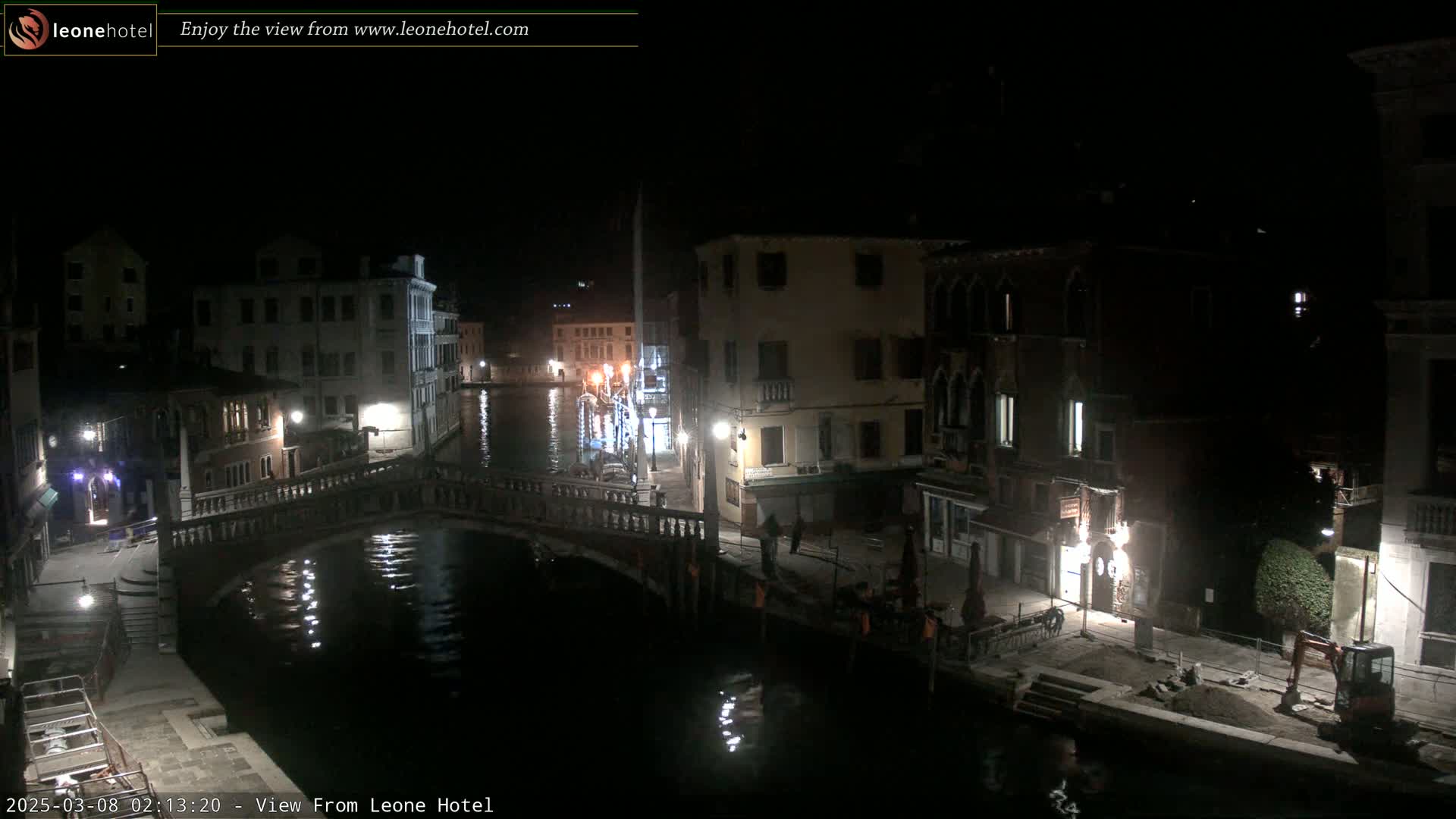 A nighttime view of a canal in Venice, Italy, shows a bridge, several buildings, and a small construction vehicle.