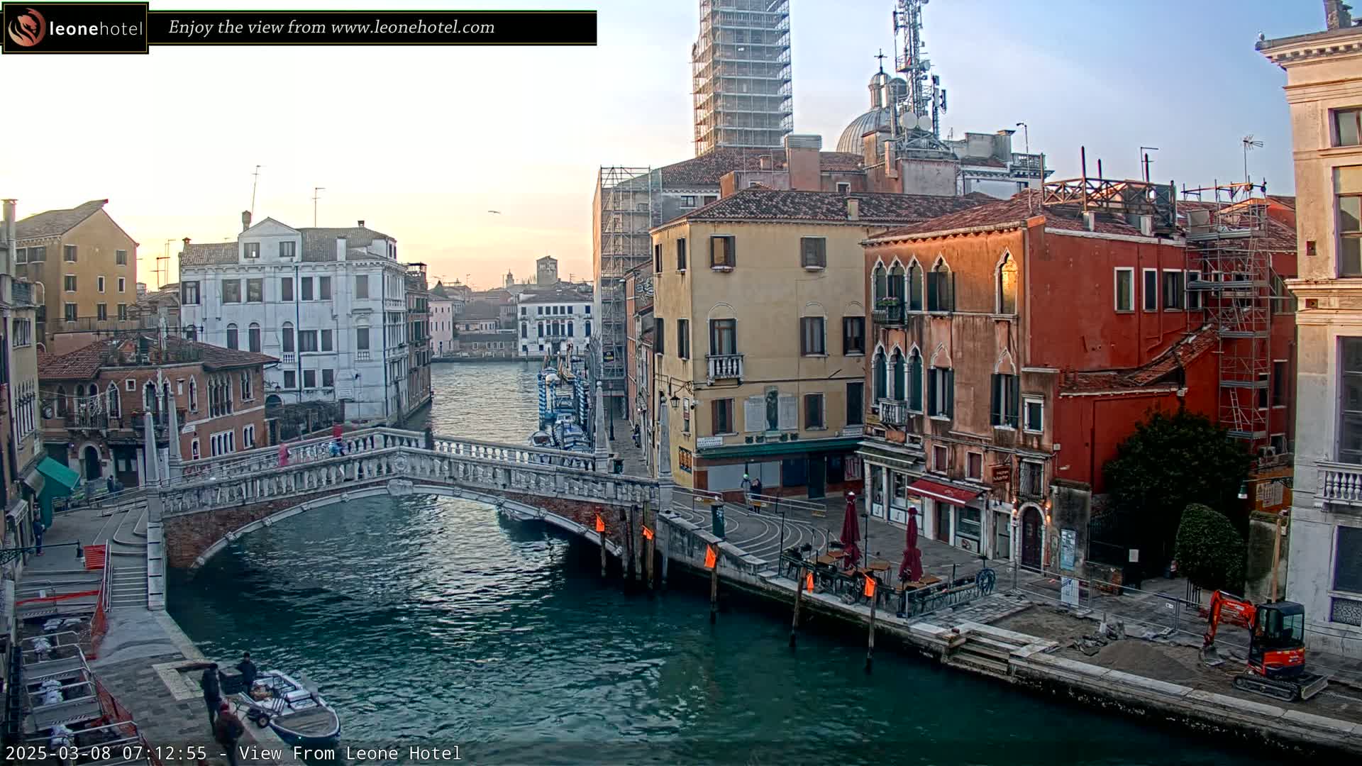 A stone bridge arches over a canal in Venice, Italy, with colorful buildings lining the waterway under a clear, twilight sky.