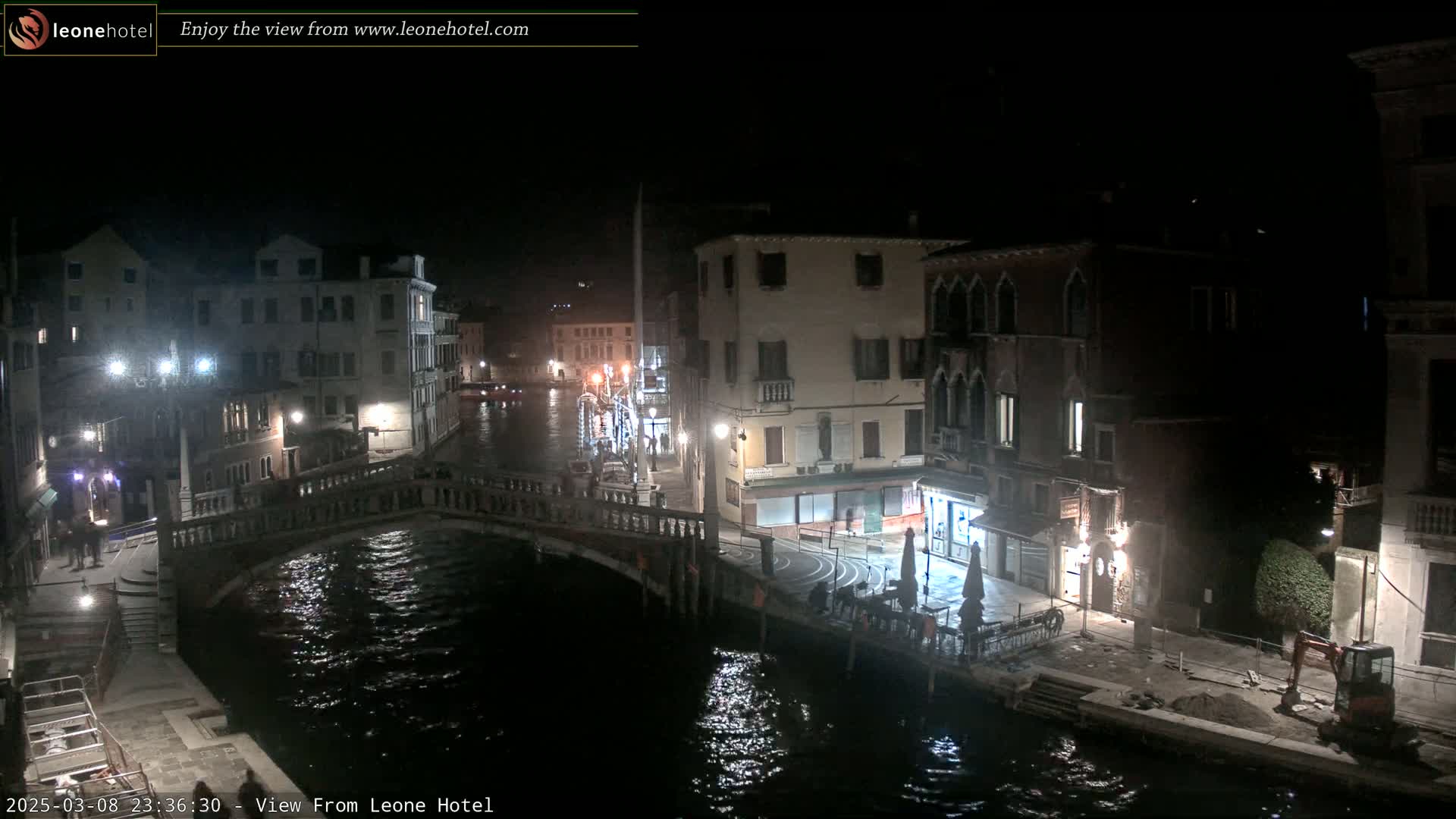 A nighttime view of a canal in Venice, Italy, showing a bridge, buildings with lights, and a small amount of construction activity.
