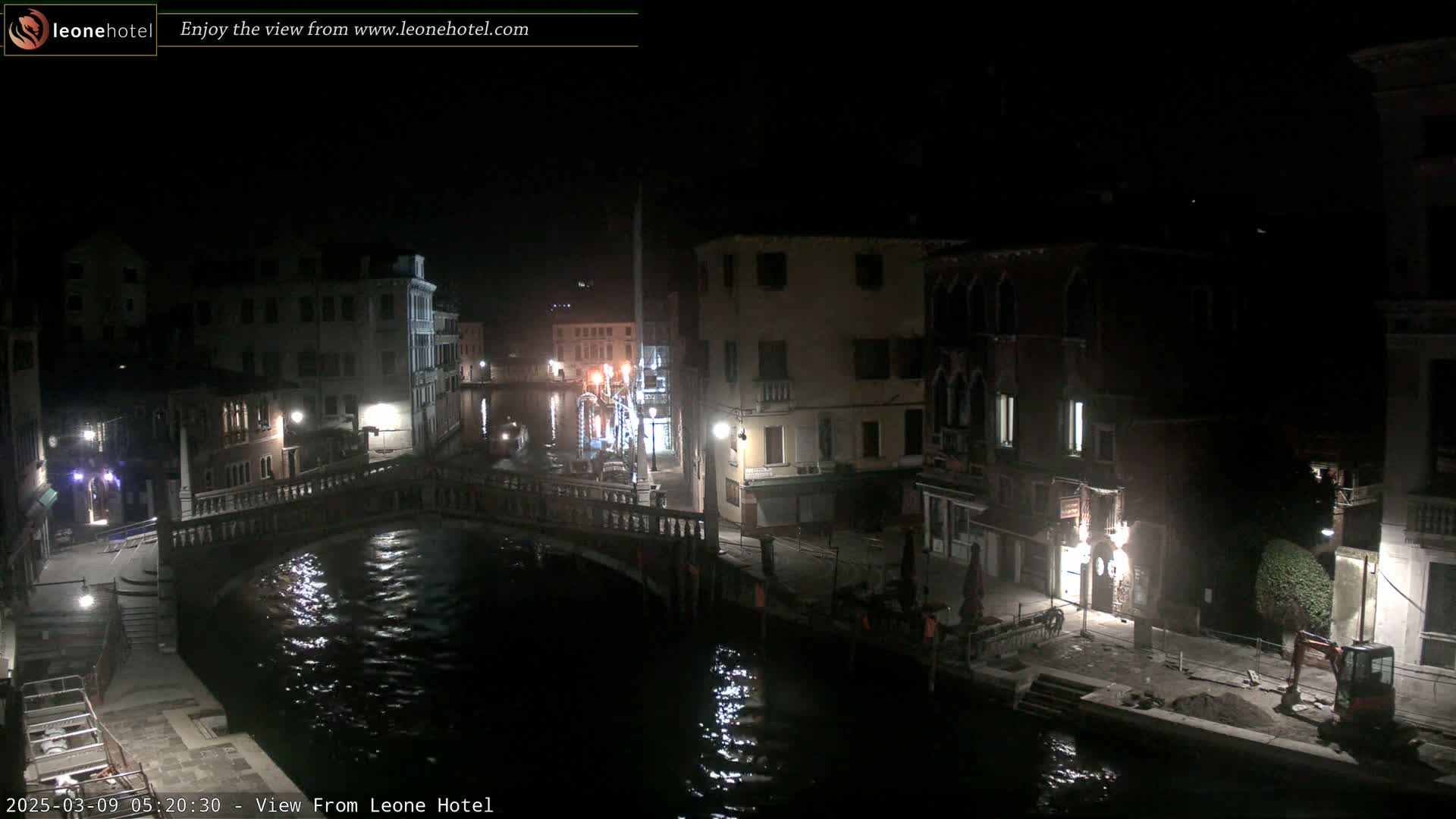 A nighttime view of a canal in Venice, with buildings lining the waterway and a bridge spanning the canal.
