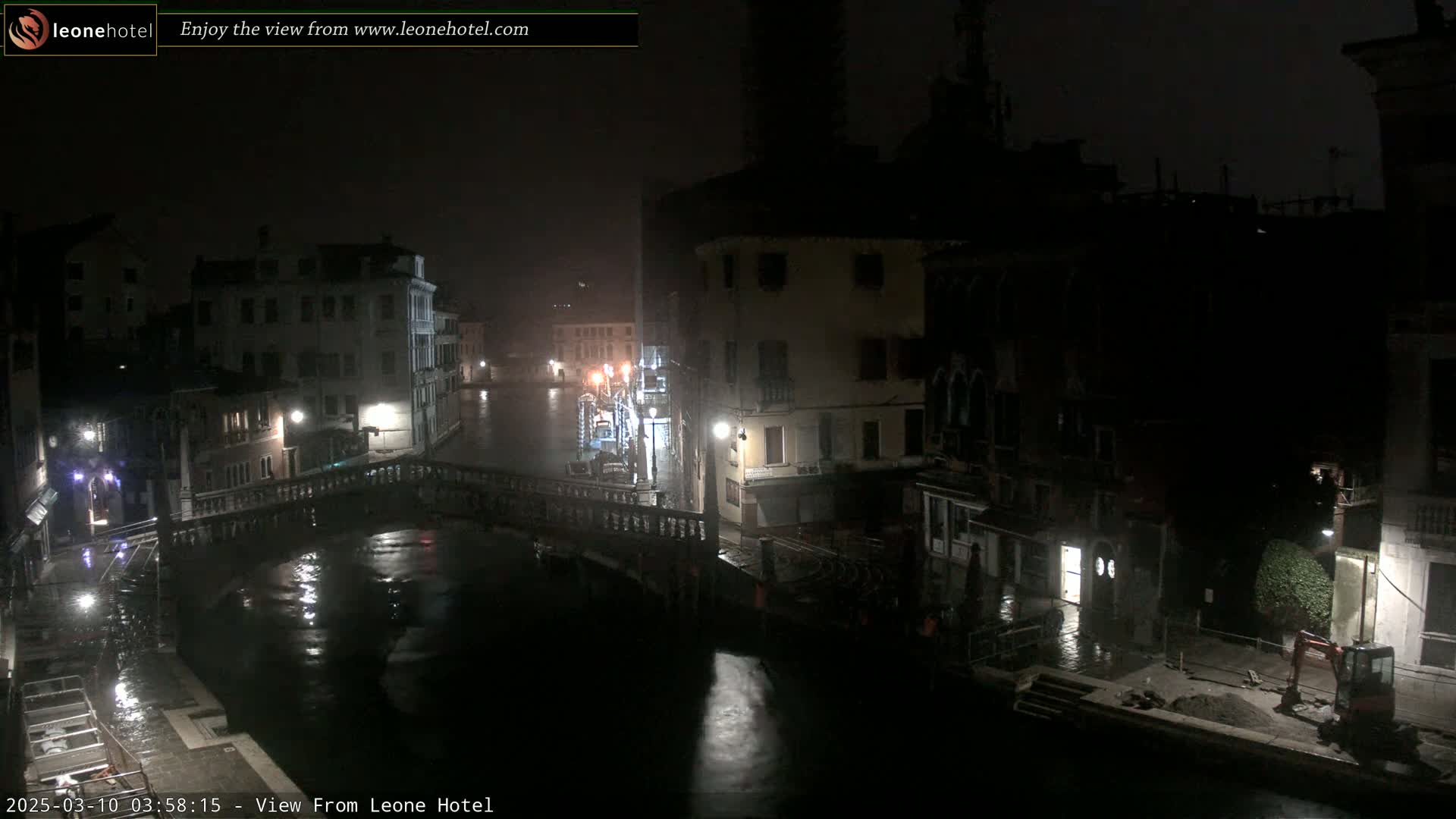 A nighttime view of a canal in Venice, Italy, showing several buildings and a bridge under rainy conditions.