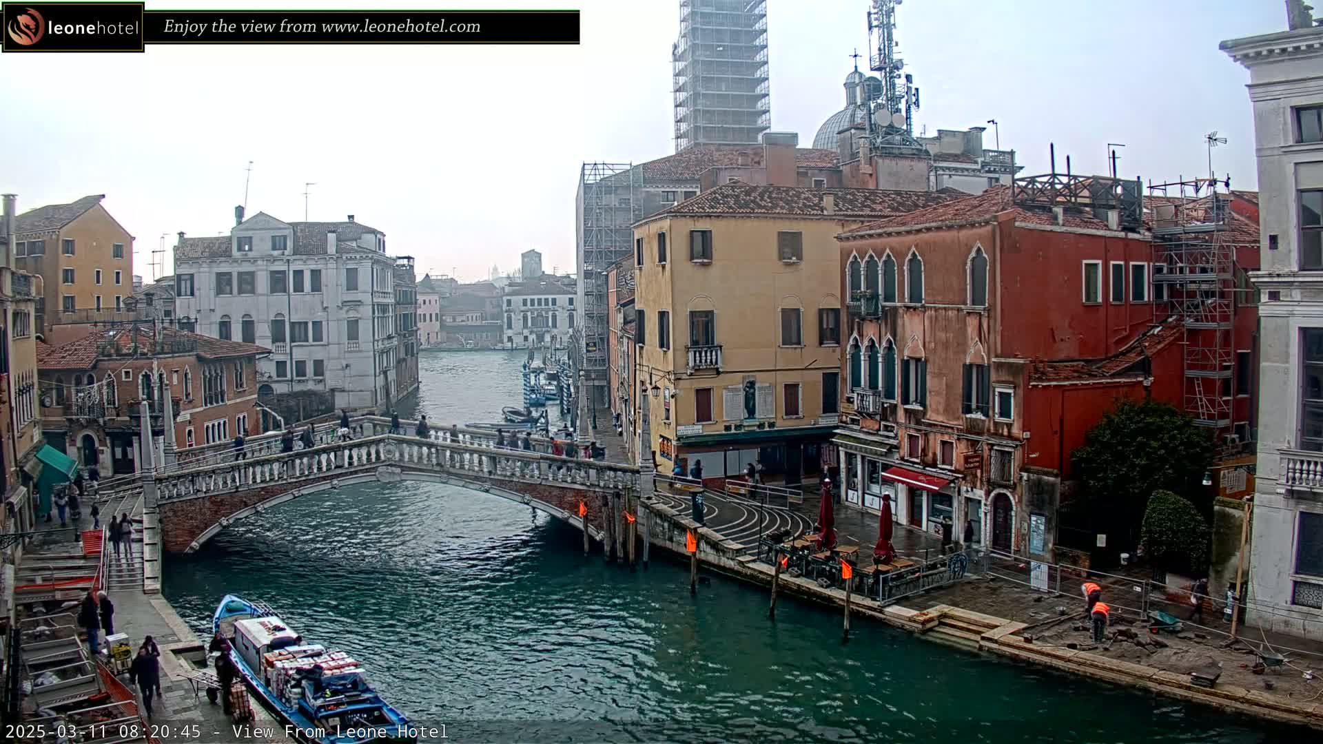 A view of a canal in Venice, Italy, on an overcast day, showing a stone bridge, several buildings, and some boats.