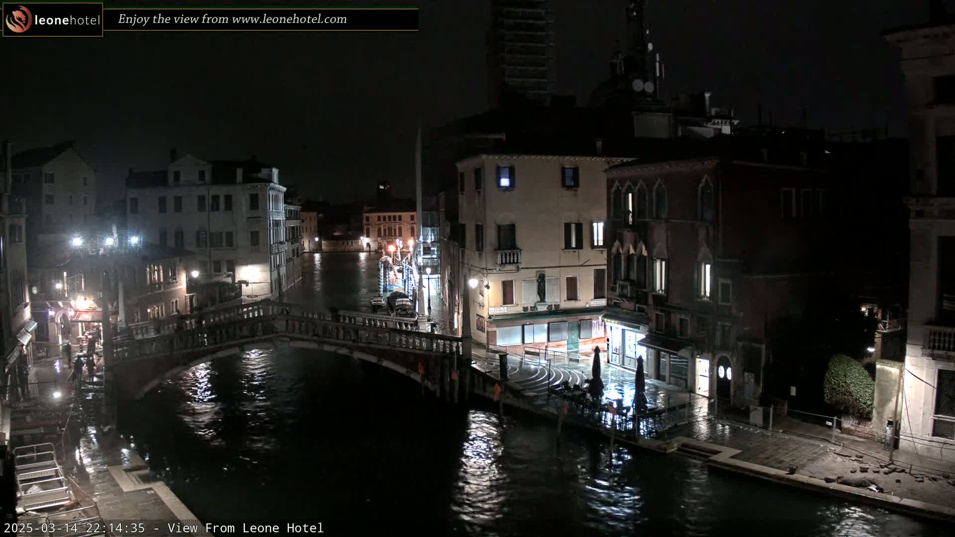A nighttime view of a canal in Venice, with water lapping at the edges of buildings and a bridge spanning the waterway.
