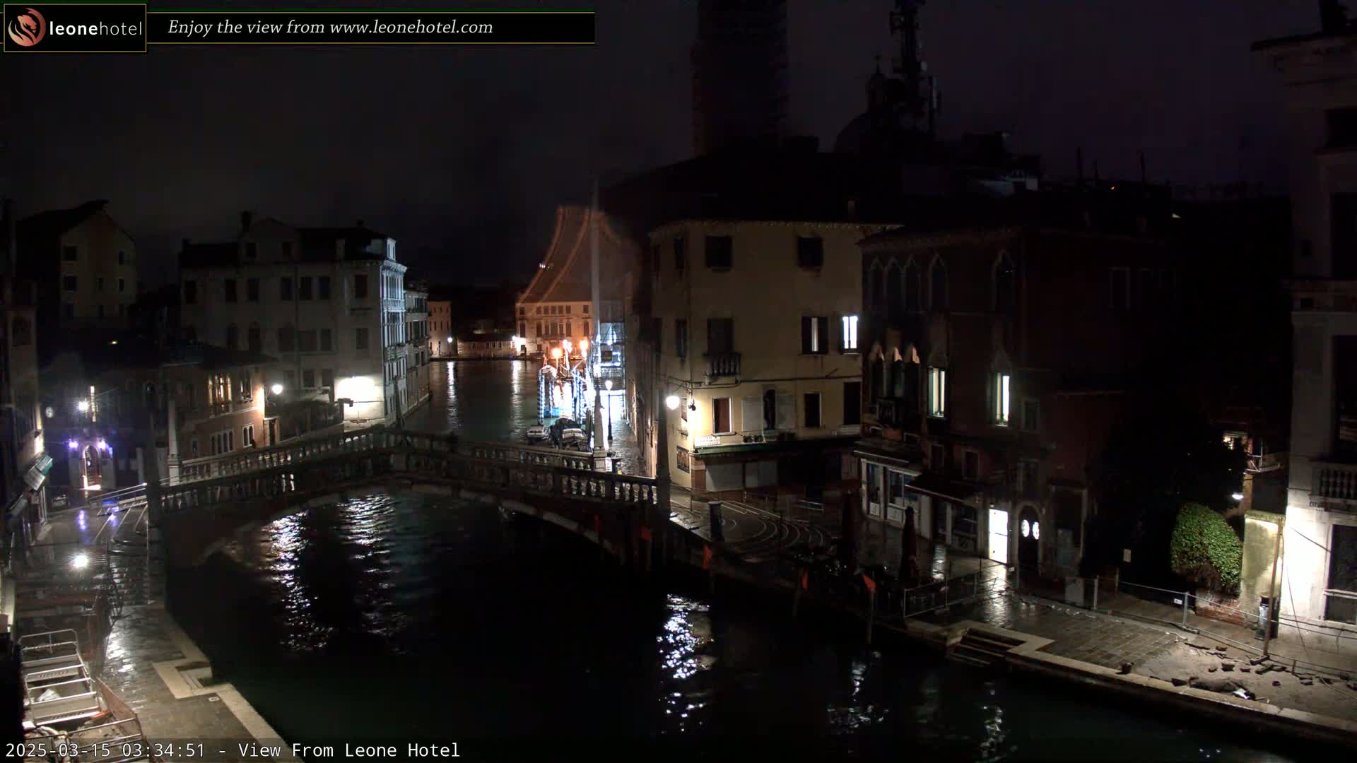 A nighttime view of a canal in Venice, showing a bridge, buildings with lights, and calm water.