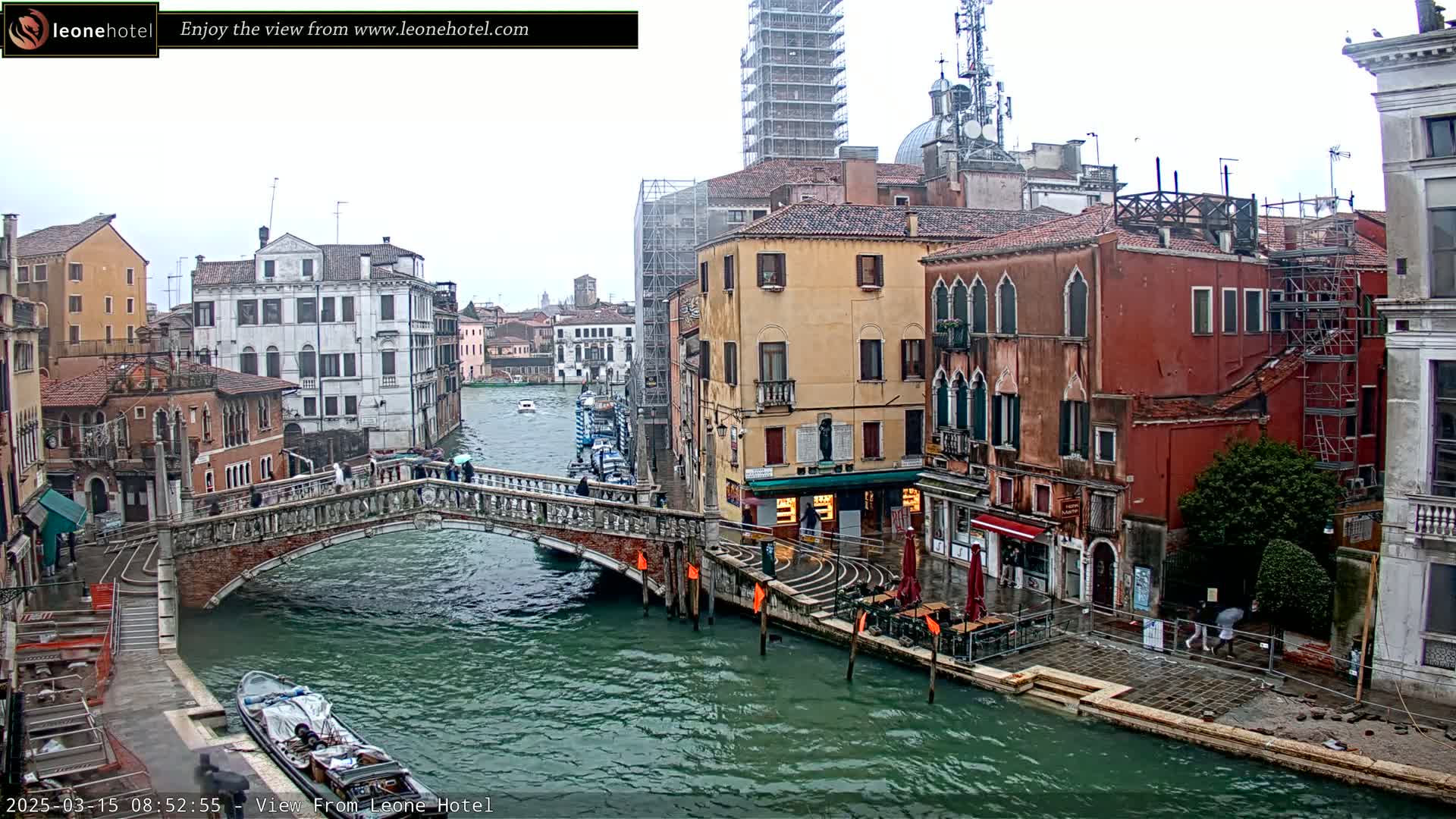 A stone bridge over a canal in Venice, Italy, on a rainy day, with several buildings lining the waterway, some under construction.