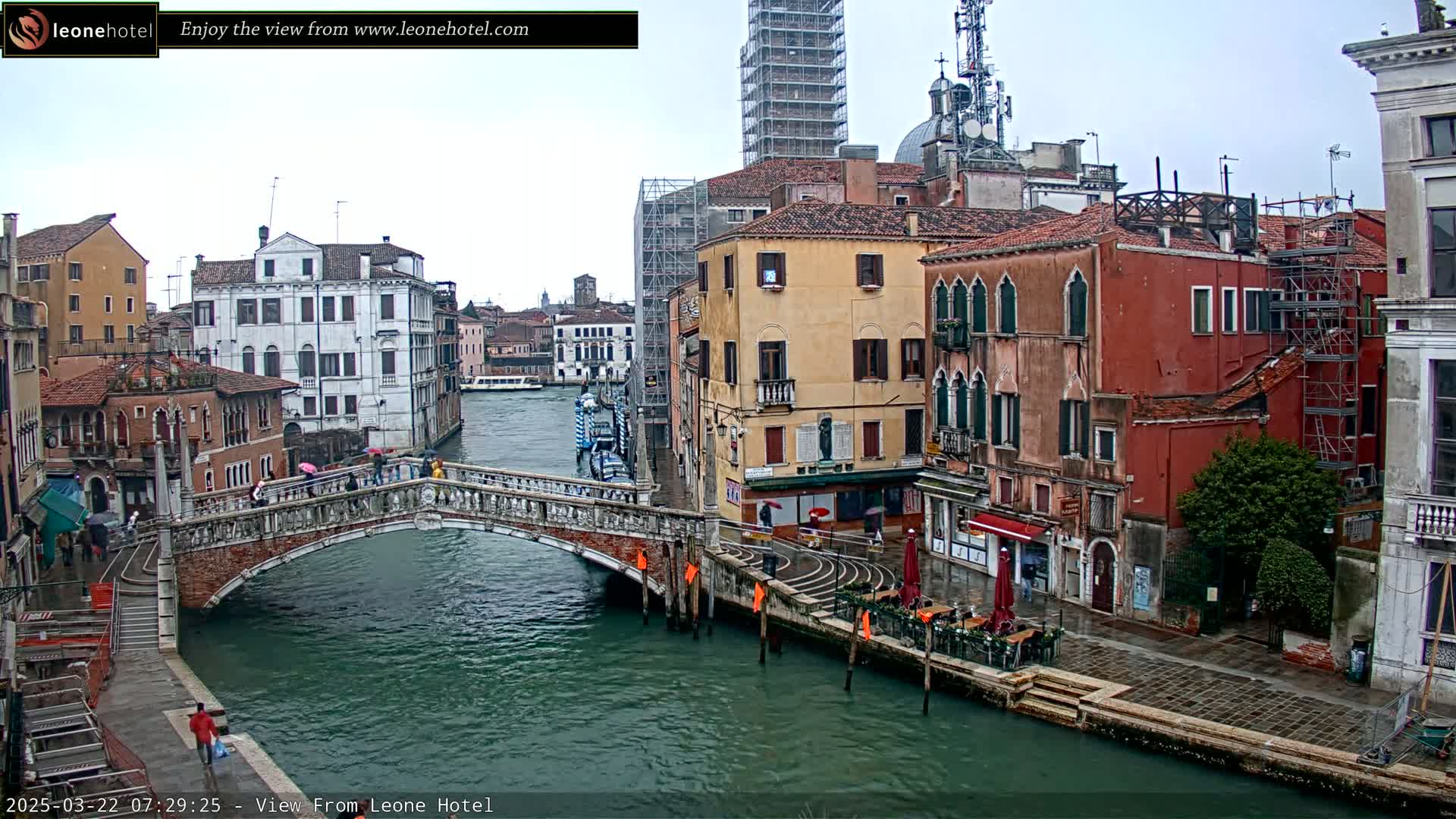 A canal in Venice, Italy, is shown on an overcast day with several buildings along its banks and a bridge crossing it.