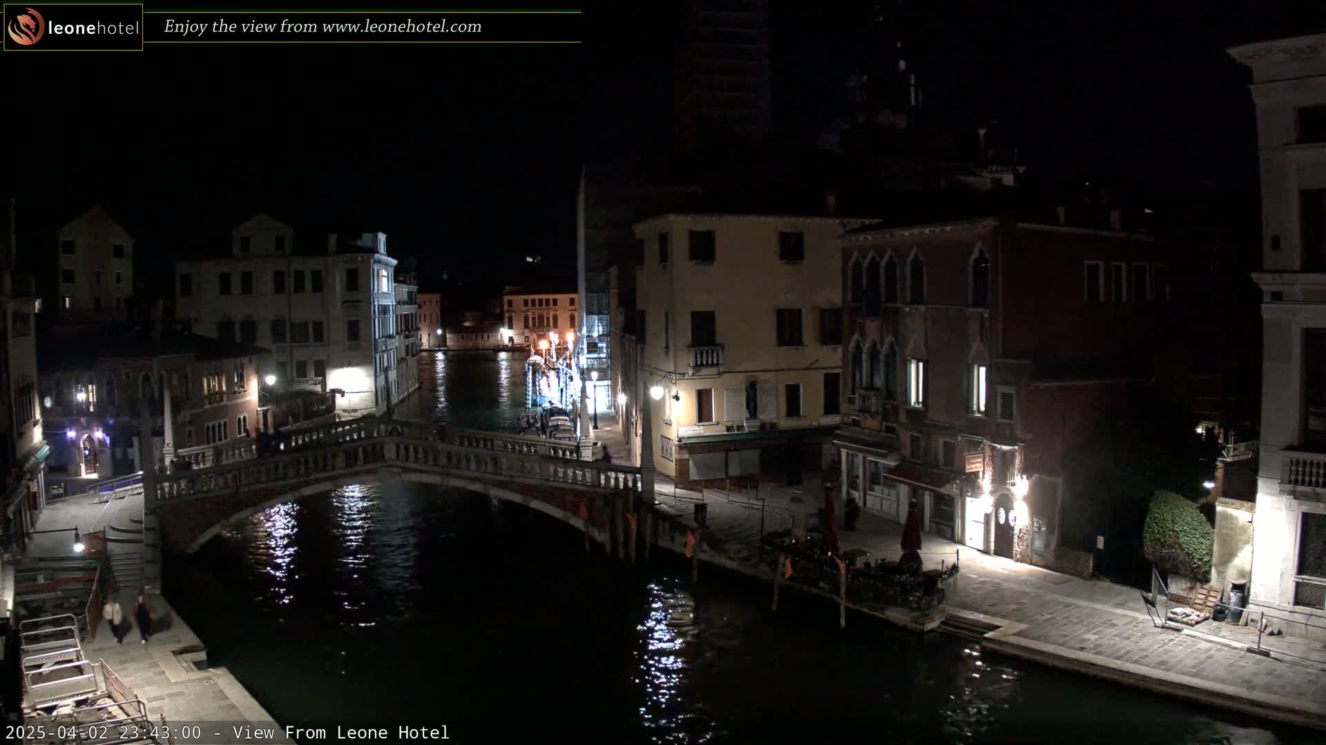 A nighttime view of a Venetian canal with a bridge, buildings lining the waterway, and some streetlights illuminating the scene.