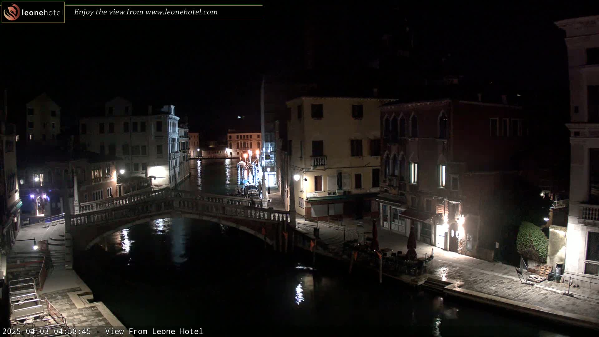 A nighttime view of a canal in Venice, with several buildings lining the waterway and a bridge crossing the canal.