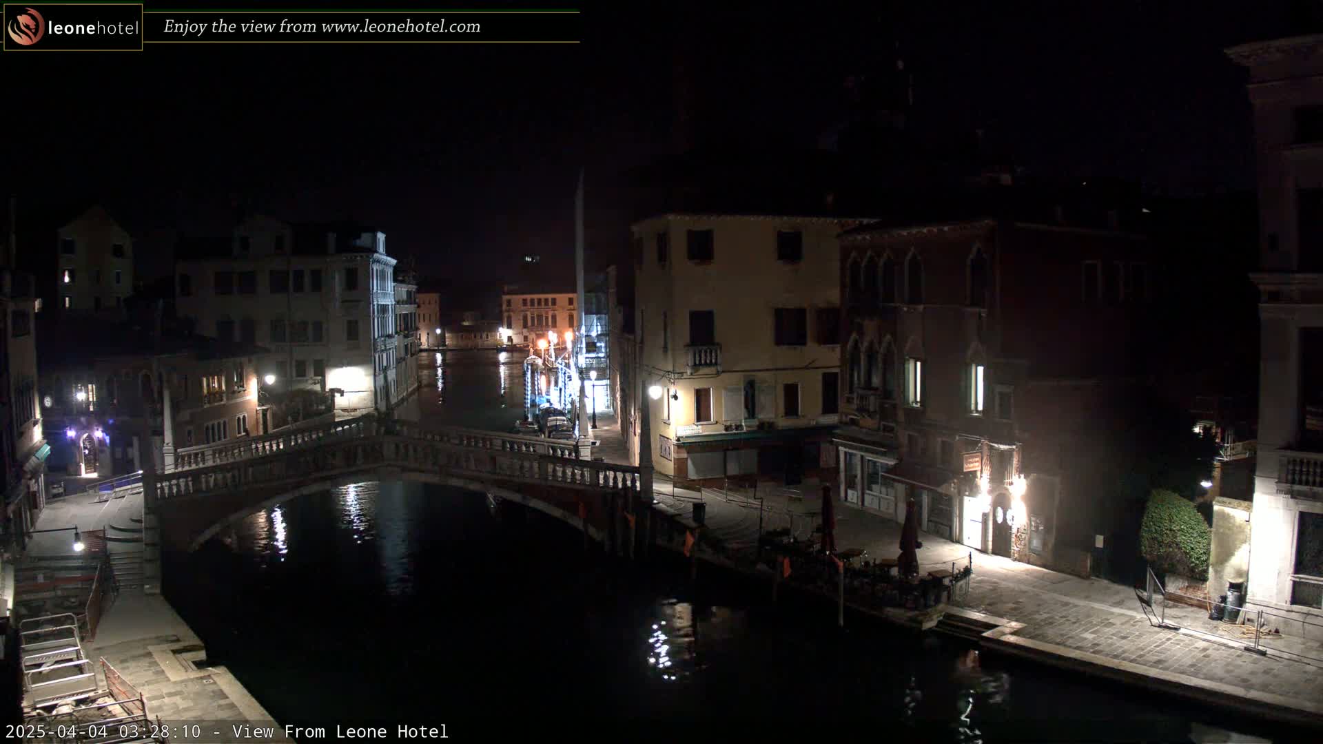 A nighttime view of a canal in Venice, with a bridge and several buildings illuminated by streetlights.