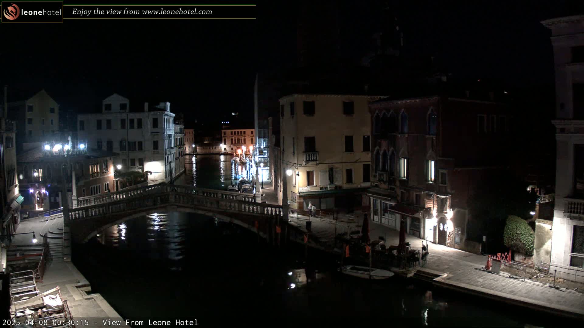 A nighttime view of a canal in Venice, with bridges, buildings, and boats, under a clear, dark sky.