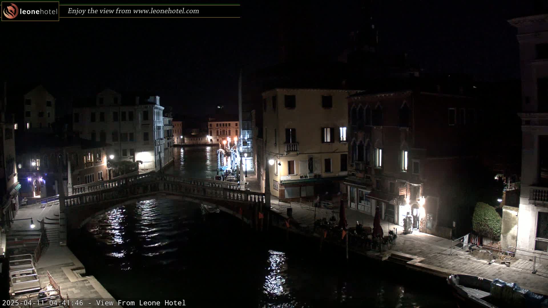 A nighttime view of a canal in Venice, Italy, shows a bridge, buildings with lights, and a calm waterway reflecting the lights.