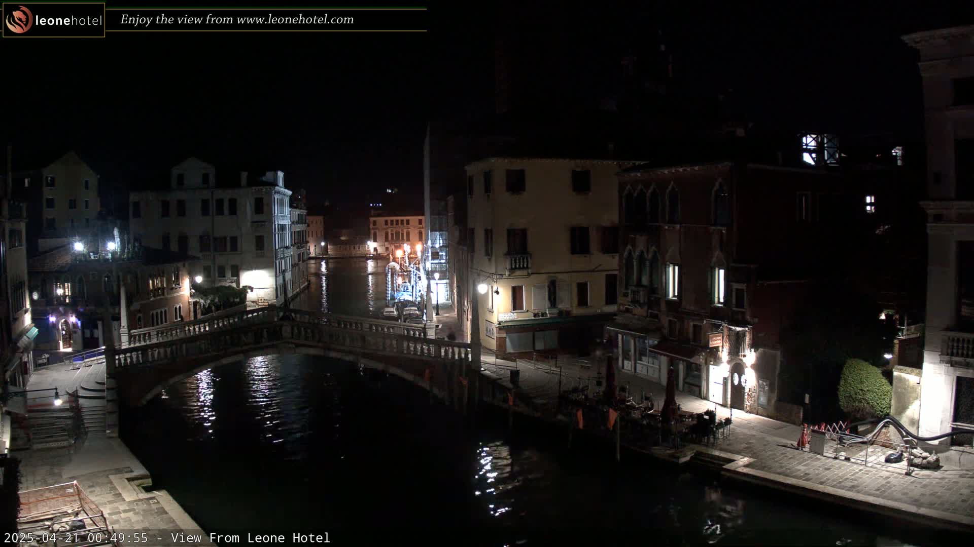 A nighttime view of a canal in Venice, Italy, shows several buildings lining the waterway with a bridge crossing the canal.
