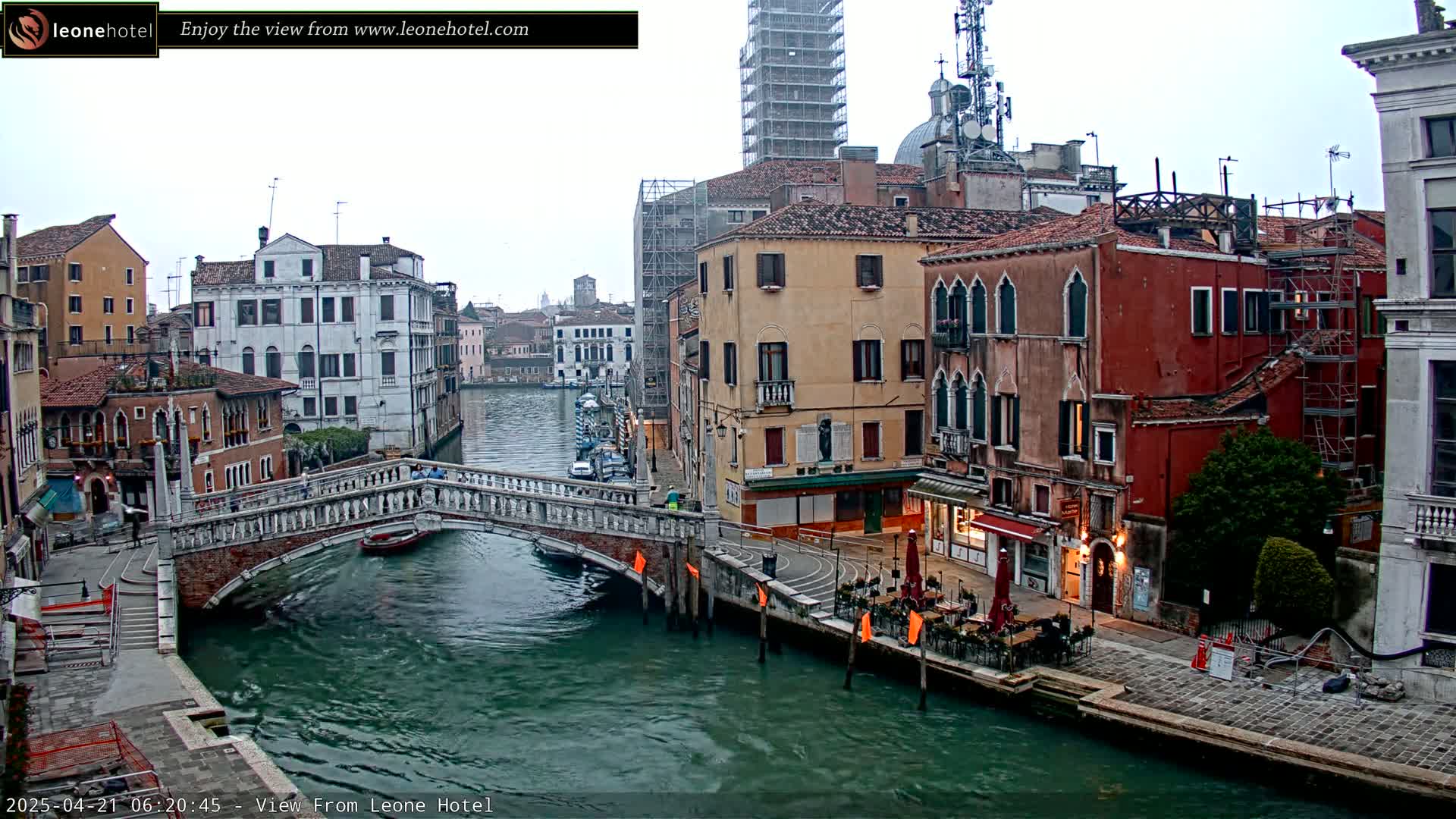 A stone bridge spans a canal in Venice, Italy, with colorful buildings lining the waterway under an overcast sky.