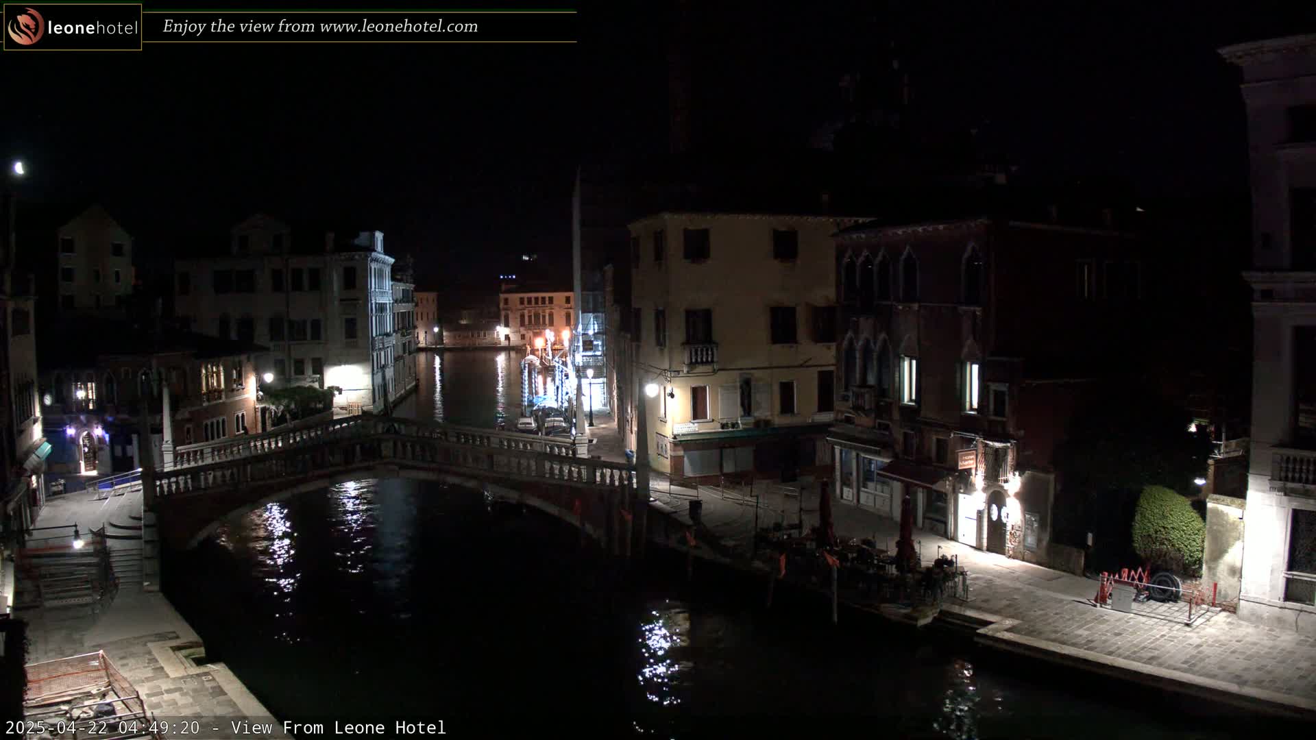 A nighttime view of a canal in Venice, with bridges, buildings, and dimly lit streets, reflecting in the calm water.