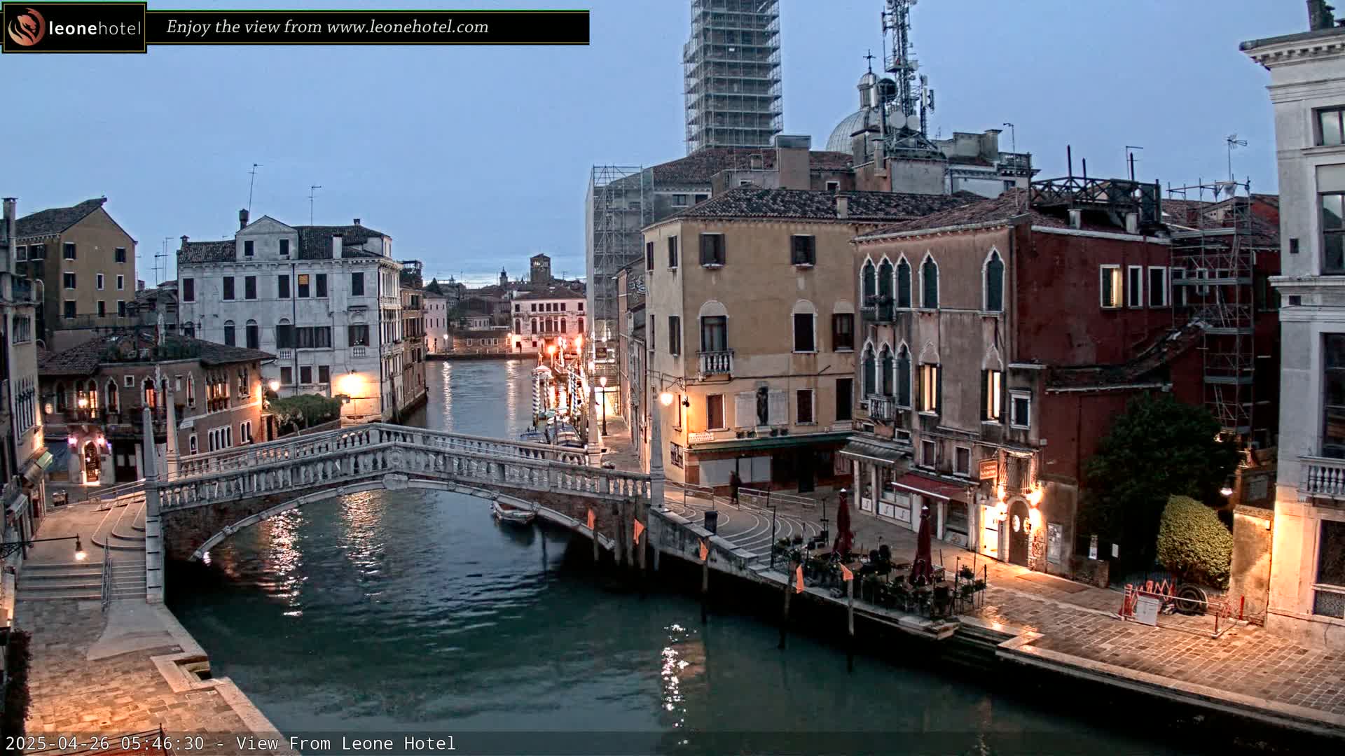 A stone bridge arches over a calm canal in Venice, under a twilight sky, with buildings lining the waterway.