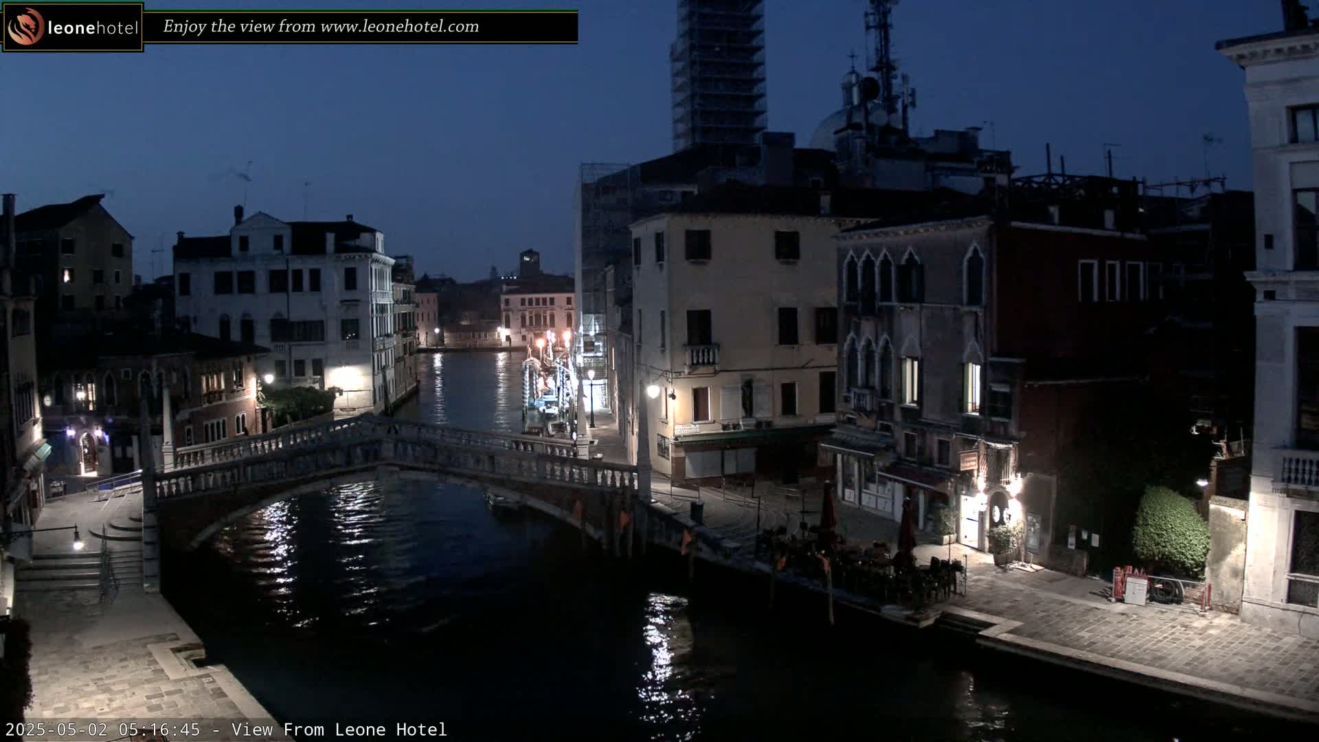 A nighttime view of a canal in Venice, Italy, showing several buildings and a bridge, under a dark, clear sky.