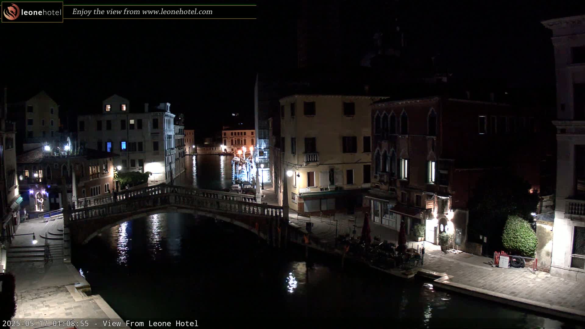 A nighttime view of a canal in Venice, showing bridges, buildings, and calm water reflecting lights.