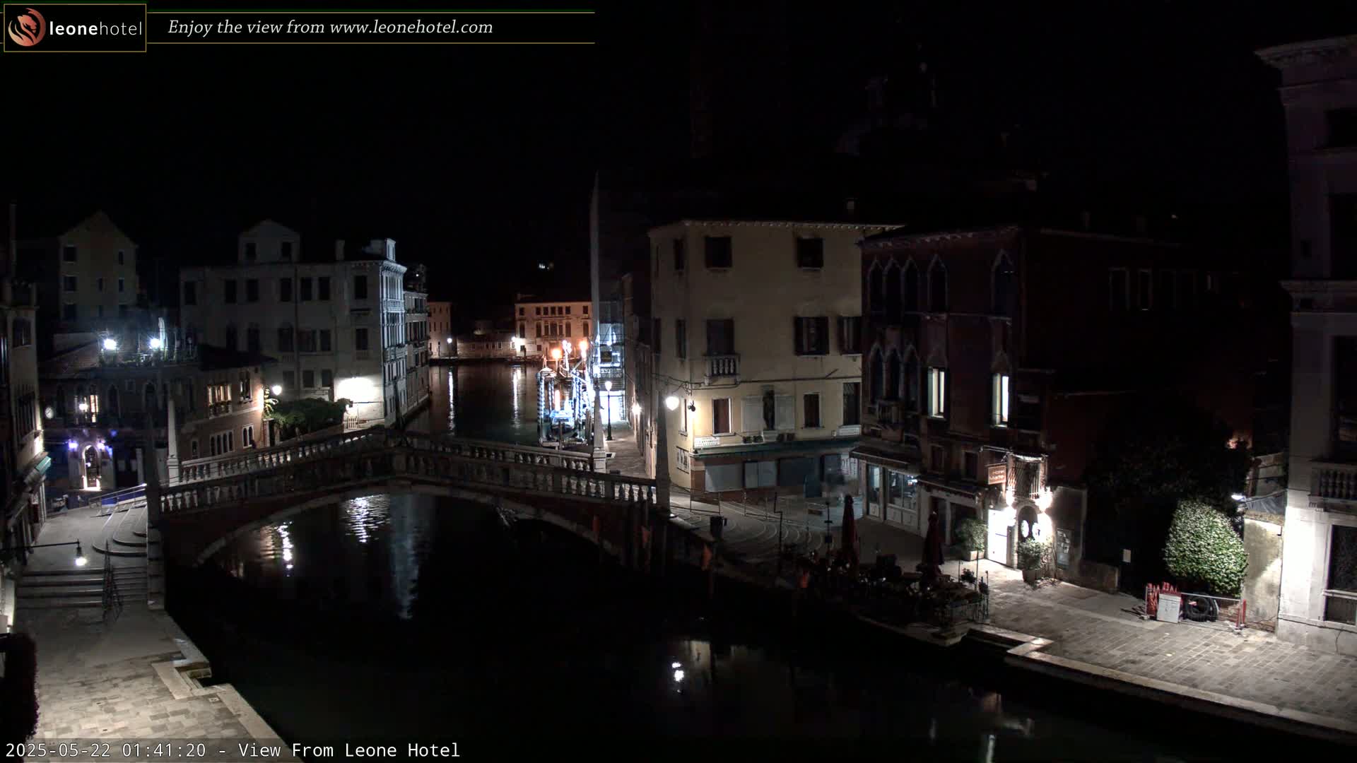 A nighttime view of a canal in Venice, Italy, shows a bridge spanning the waterway, with buildings lining both sides, softly lit by streetlights.