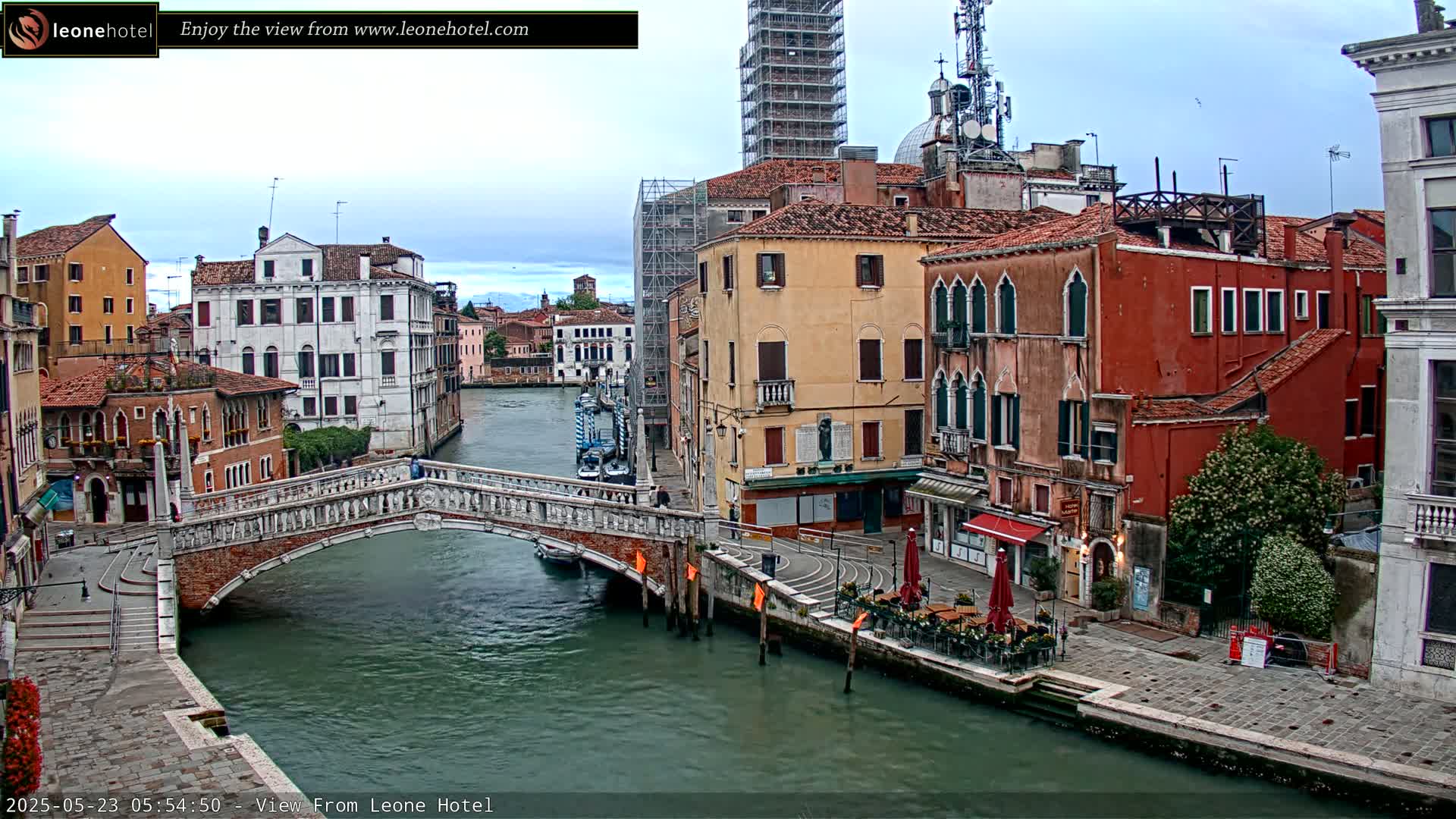 A stone bridge arches over a canal in Venice, Italy, under an overcast sky, with colorful buildings lining the waterway.