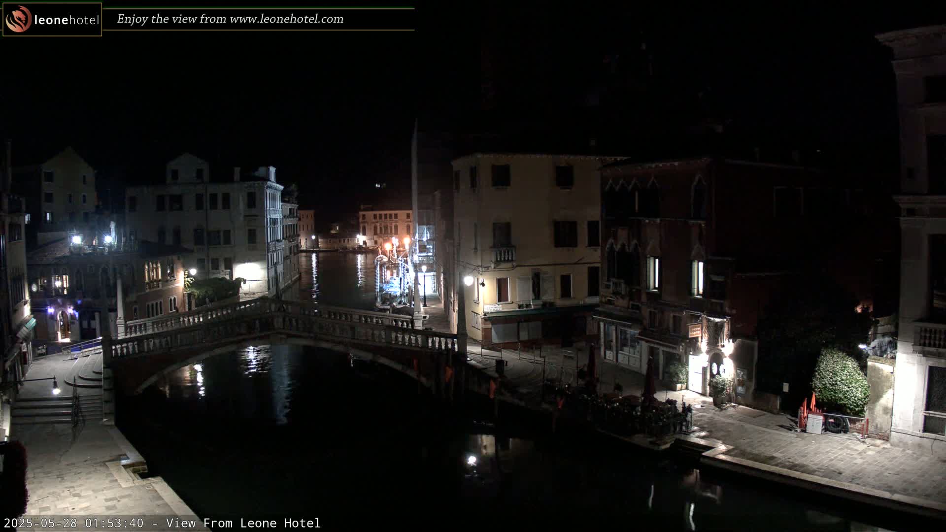 A nighttime view of a canal in Venice, Italy, shows several buildings illuminated along the waterway with a bridge spanning the canal.