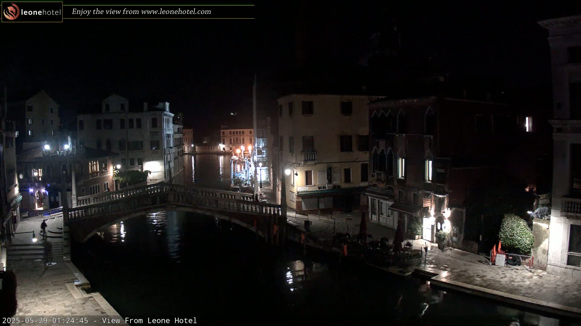 A nighttime view of a canal in Venice, showing several buildings and a bridge, with calm water reflecting the lights.