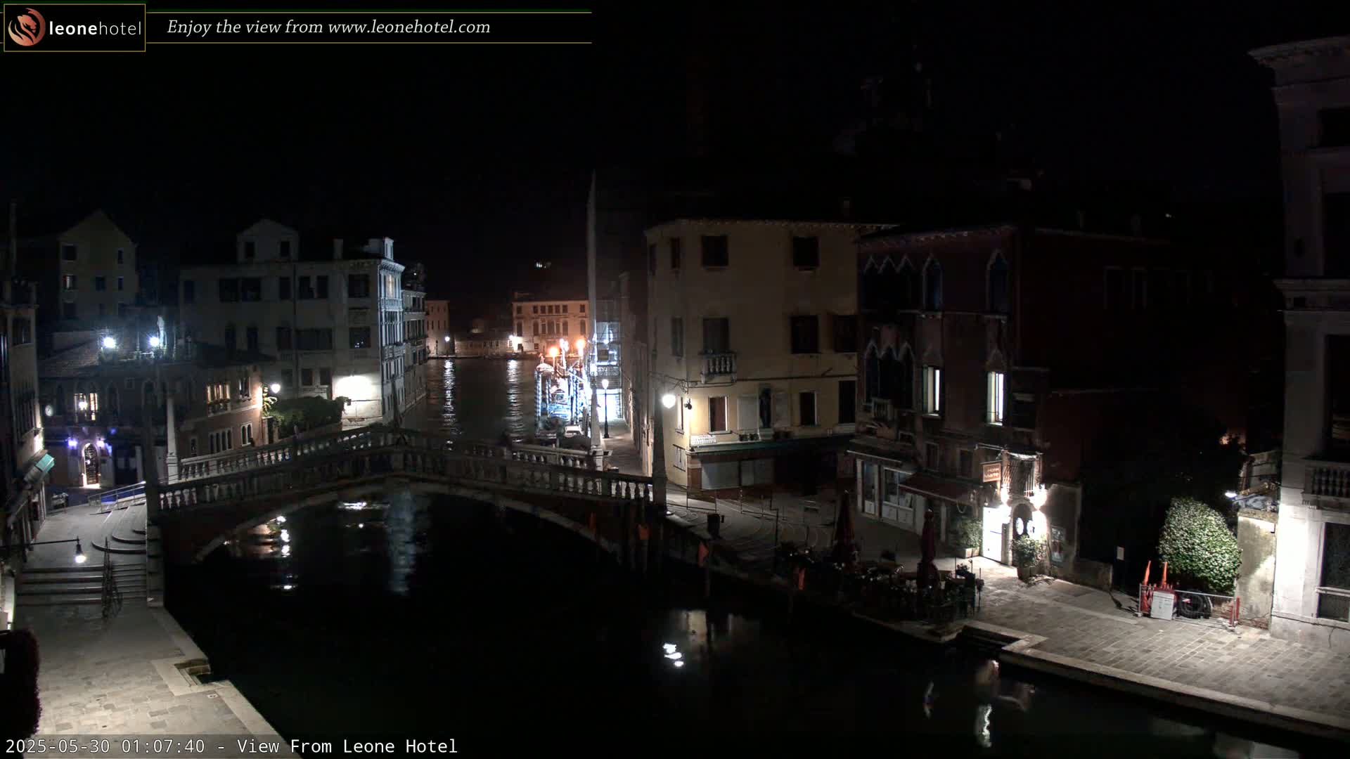 A nighttime view of a canal in Venice, Italy, shows several buildings lining the waterway, with a bridge spanning the canal, under a clear, dark sky.