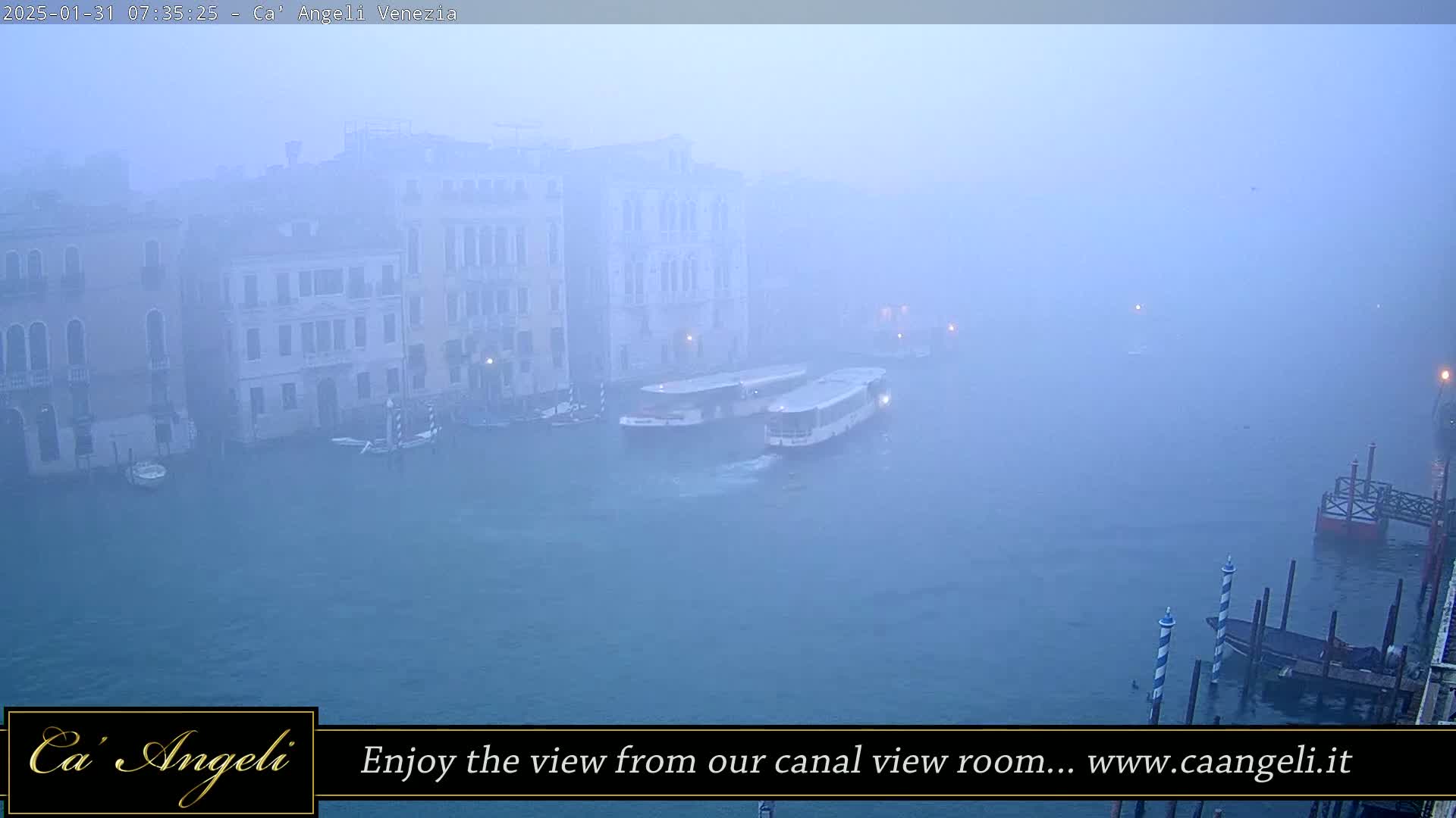 Two boats are moored on a foggy canal in Venice, with buildings lining the waterway.