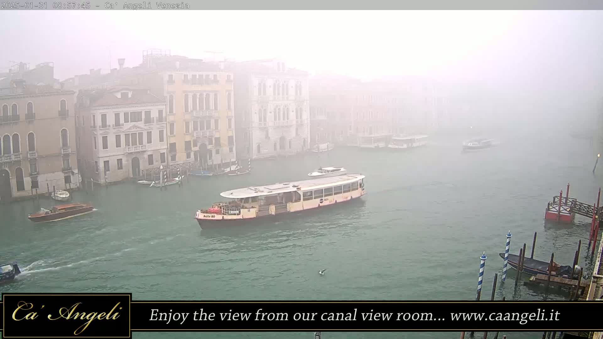 A canal in Venice, shrouded in fog, shows several boats and buildings along its banks.