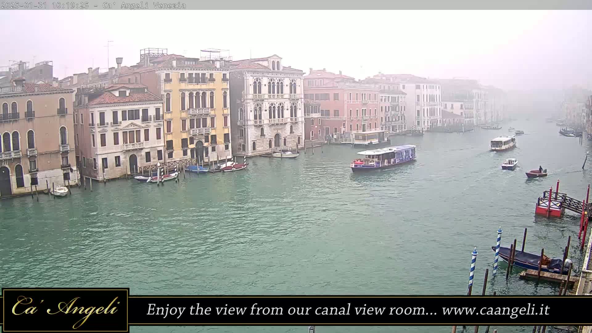 A foggy view of a canal in Venice, Italy, shows several buildings along the waterway, with boats of various sizes moving on the water.